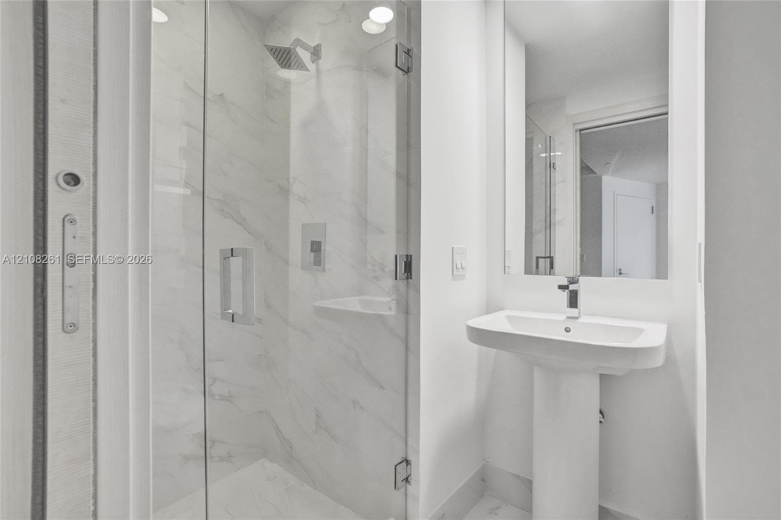 Walk-in shower with floor-to-ceiling stone-style tile and glass enclosure, integrated shower bench, rainfall showerhead, and pedestal sink with chrome faucet