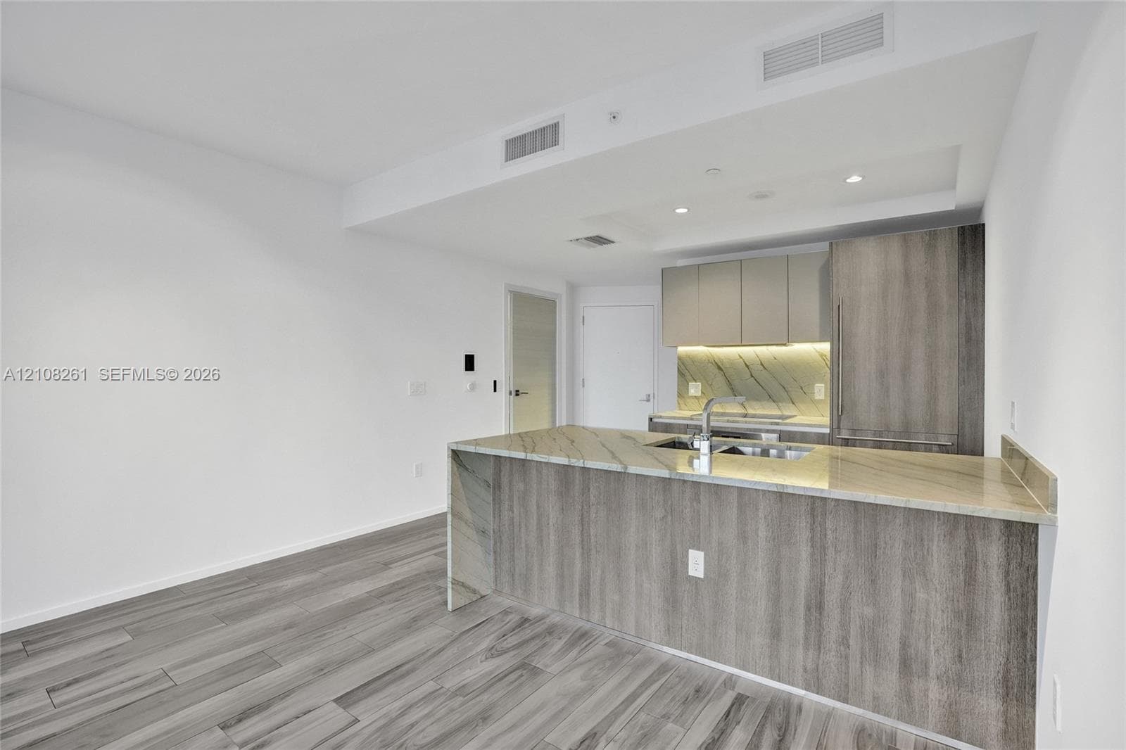Kitchen featuring wood-finish cabinetry, stone-surface waterfall island with an integrated sink, stone backsplash, and wood-finish flooring