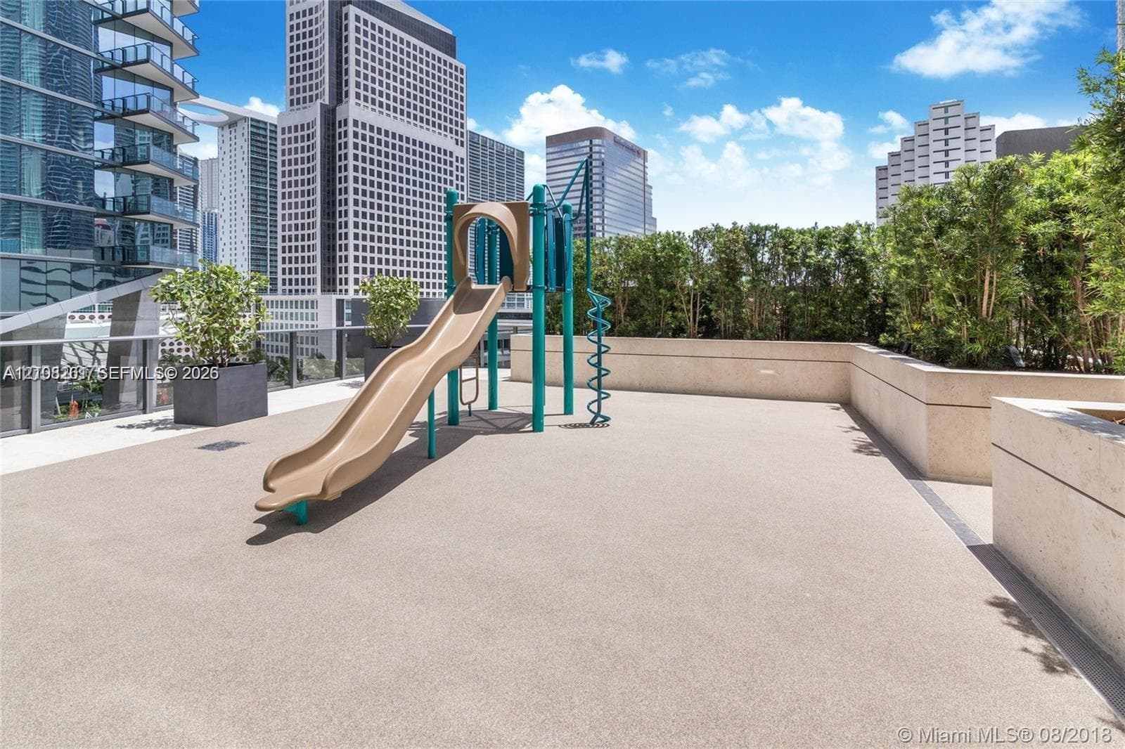 Outdoor terrace featuring a built-in playground slide, perimeter masonry walls, planters, and high-rise cityscape surroundings