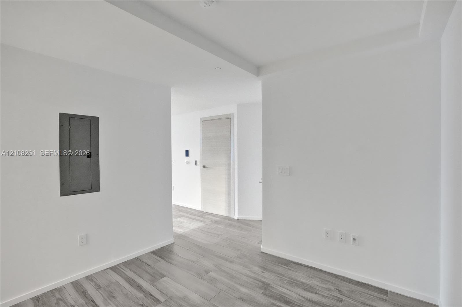 Neutral interior featuring light wood-finish flooring, smooth white walls, recessed ceiling lighting, and a textured interior door with satin nickel hardware