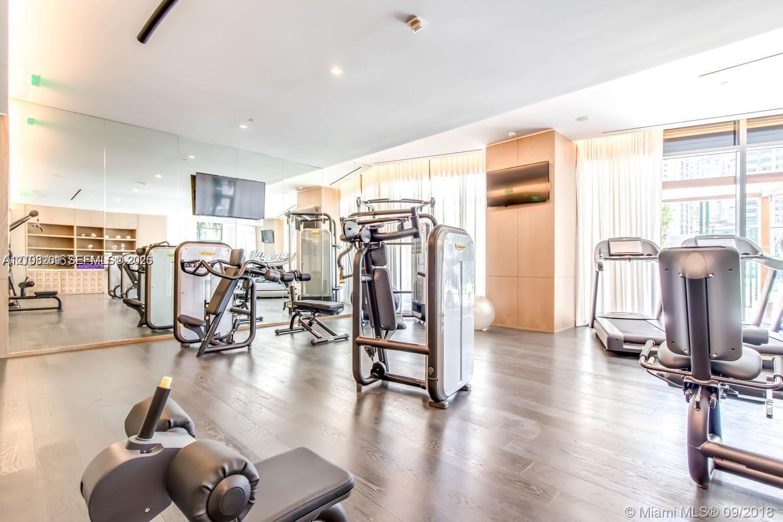 Fitness area featuring wood-finish flooring, full-length wall mirrors, recessed lighting, and expansive floor-to-ceiling windows