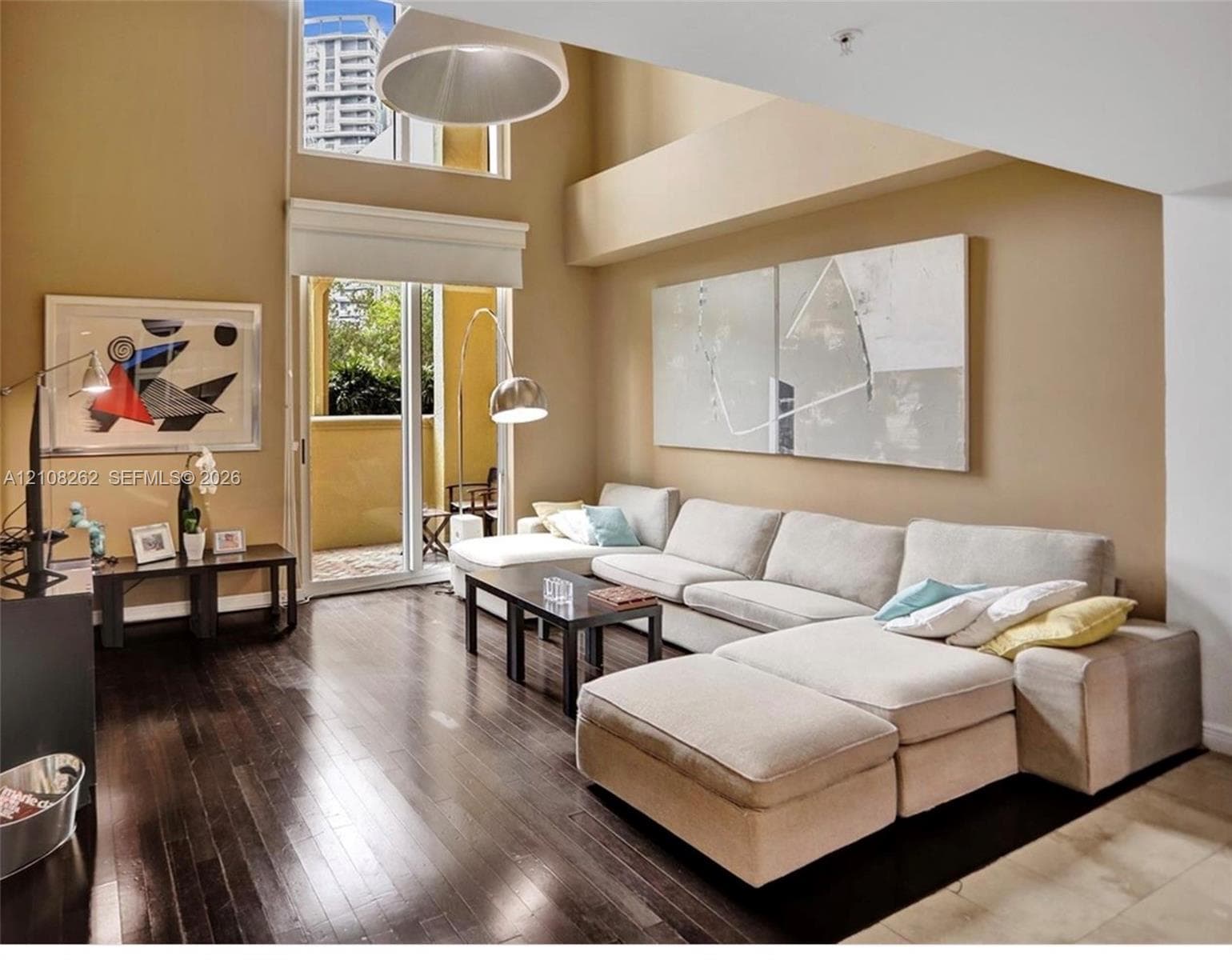 Double-height ceilings featuring an expansive clerestory window, wood-finish flooring, and sliding glass doors leading to a private balcony