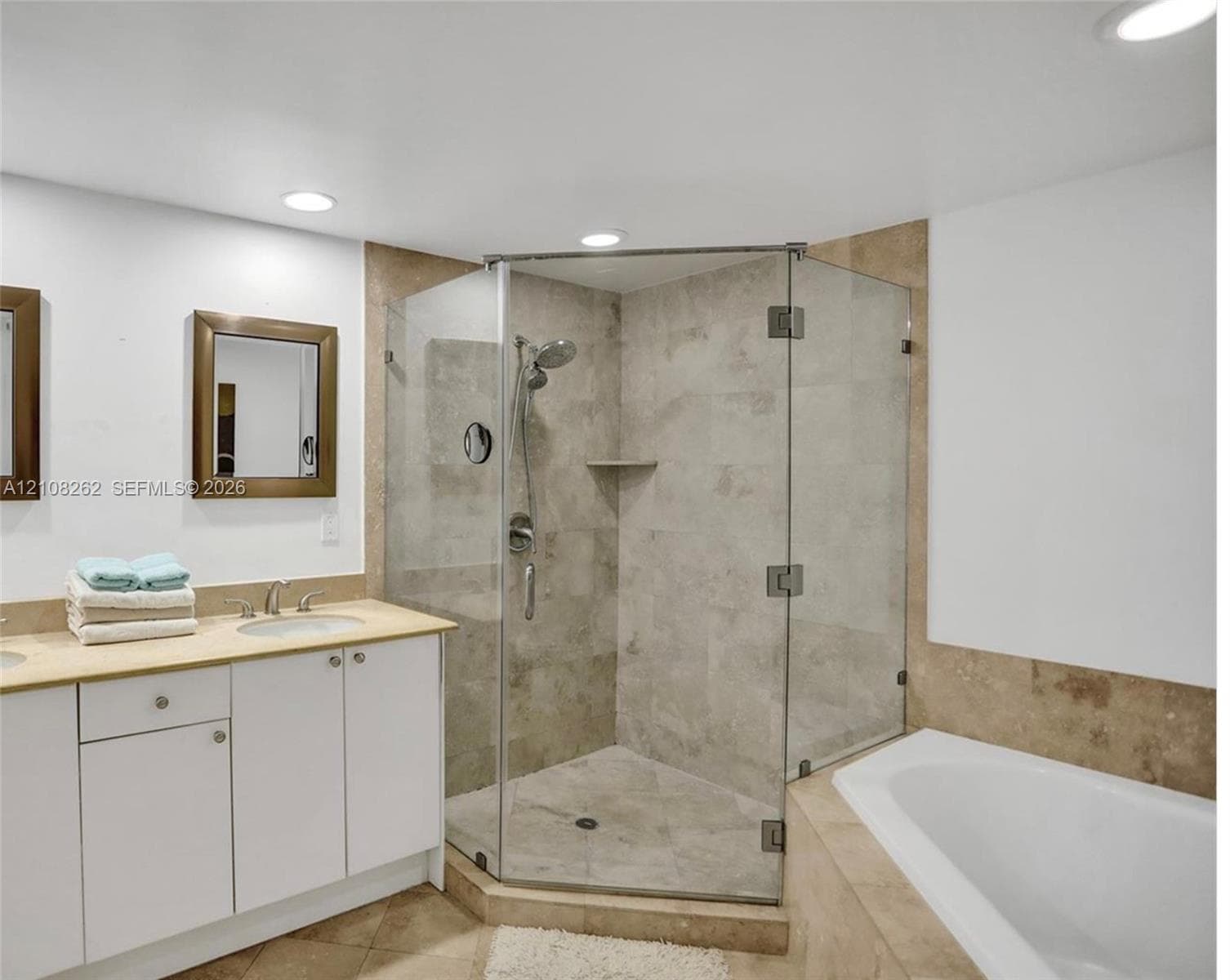 Corner glass-enclosed shower with tile surround, built-in soaking tub, stone-topped vanity with undermount sink, and recessed lighting