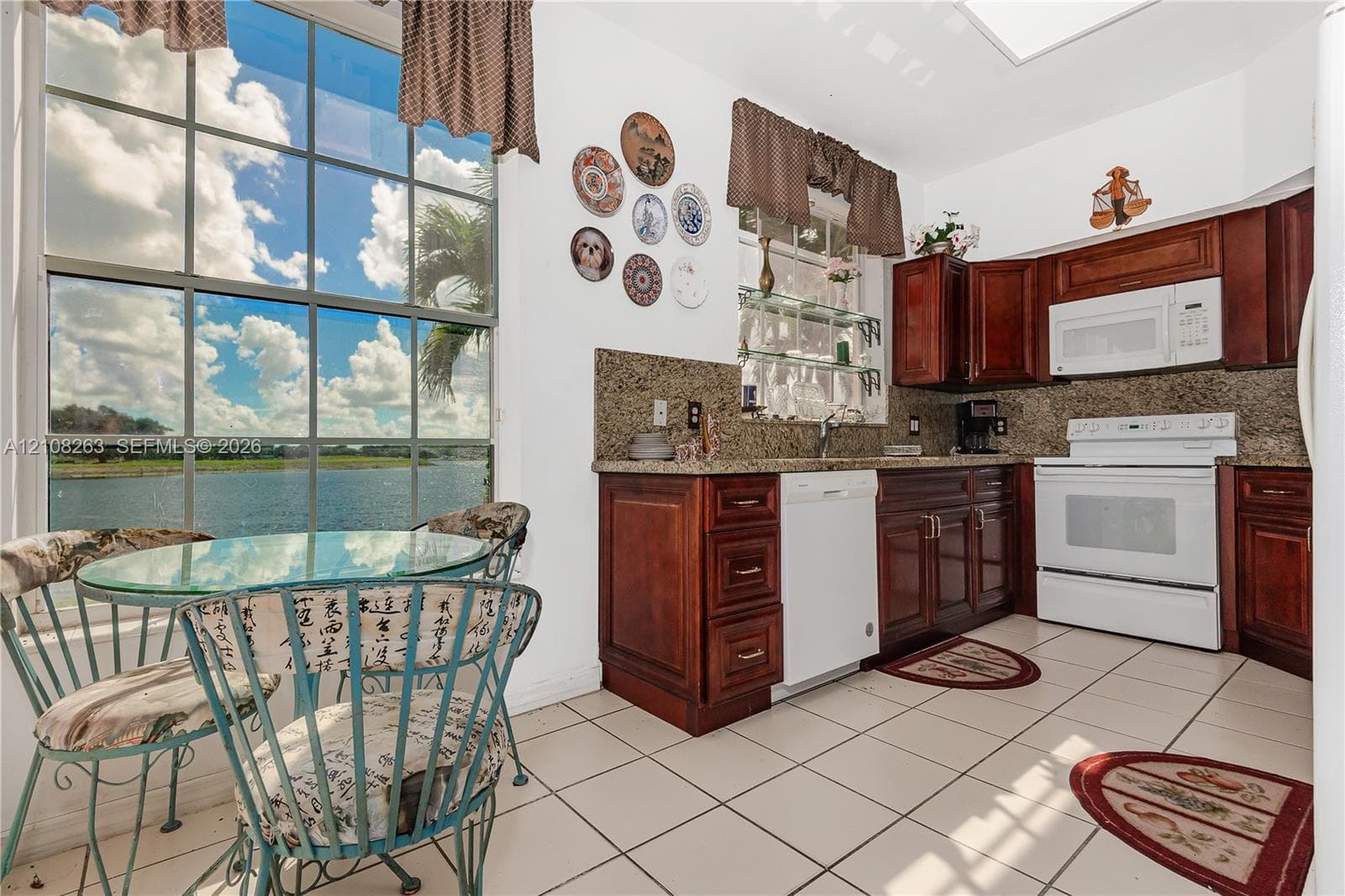 Kitchen featuring raised-panel wood cabinetry, stone countertops, tiled flooring, and floor-to-ceiling windows with water scenery