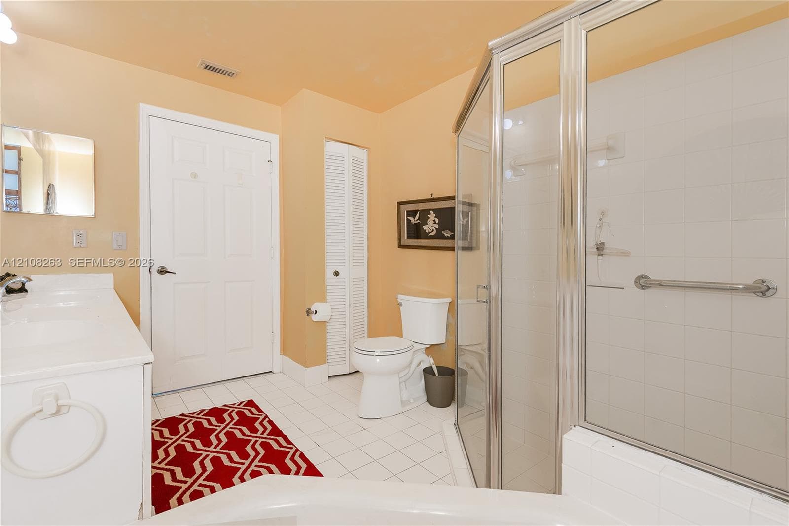 Bathroom featuring a white vanity with a composite countertop, a corner glass-enclosed shower, ceramic tile flooring, and a louvered closet door