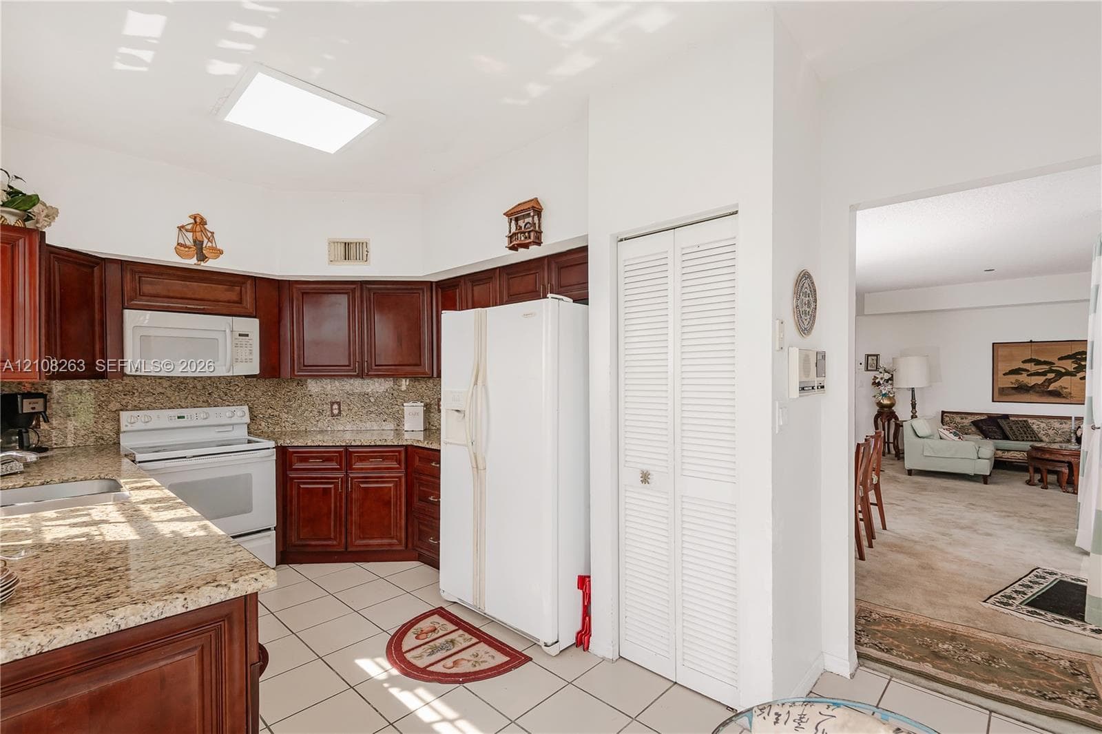 Kitchen featuring dark wood cabinetry, stone-surface countertops, tile flooring, and a recessed skylight