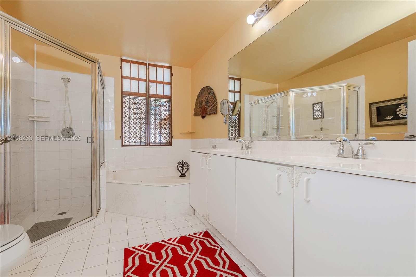 Bathroom featuring a double-sink vanity with white cabinetry, a glass-enclosed shower, a corner jetted soaking tub, large wall-mounted mirror, and tile flooring