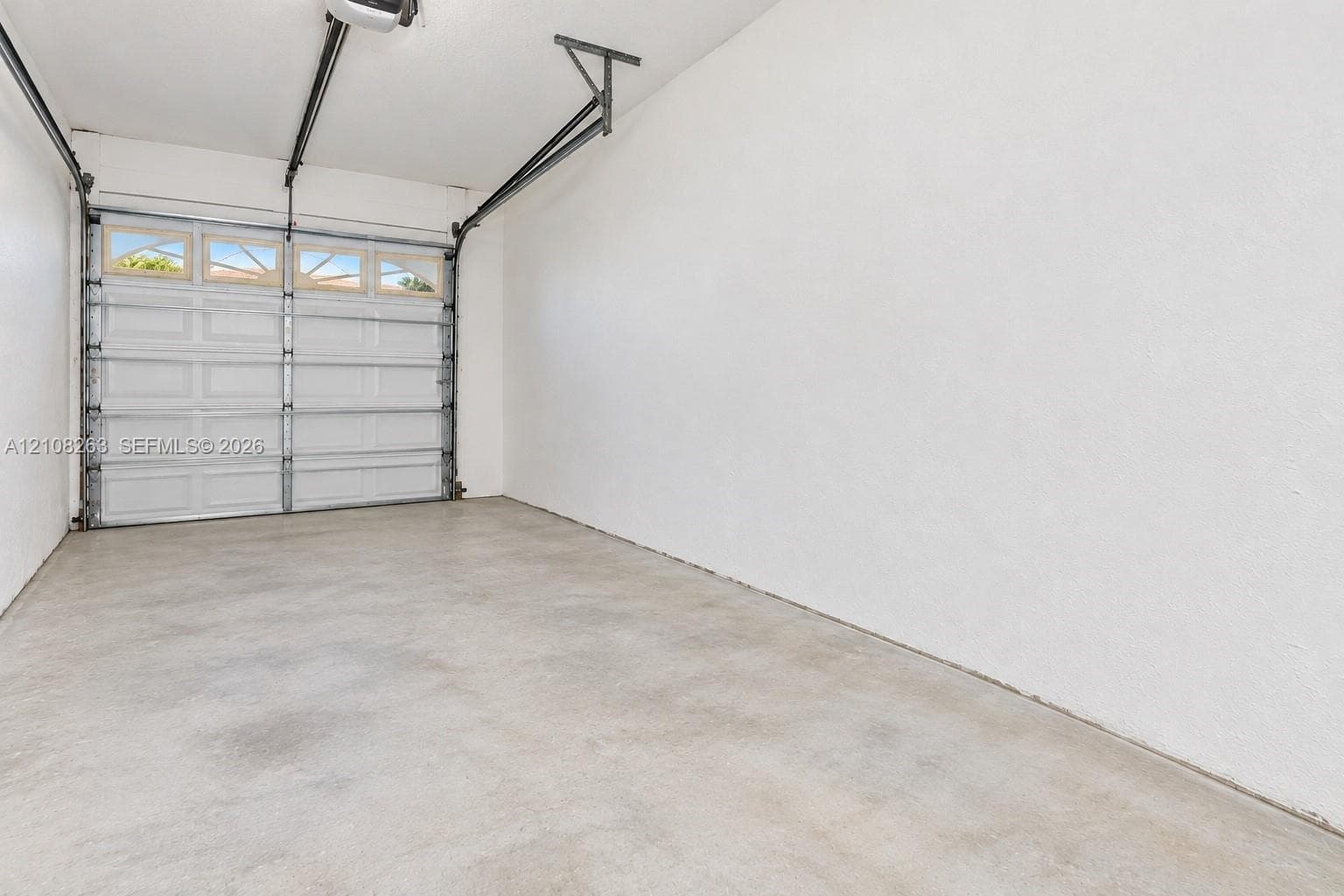 Enclosed garage featuring finished white walls, a concrete floor, and an overhead sectional door with integrated glazing panels