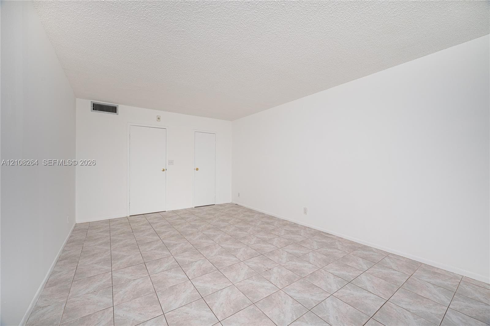 Neutral-toned tile flooring, textured ceiling, and dual interior doors finished in white