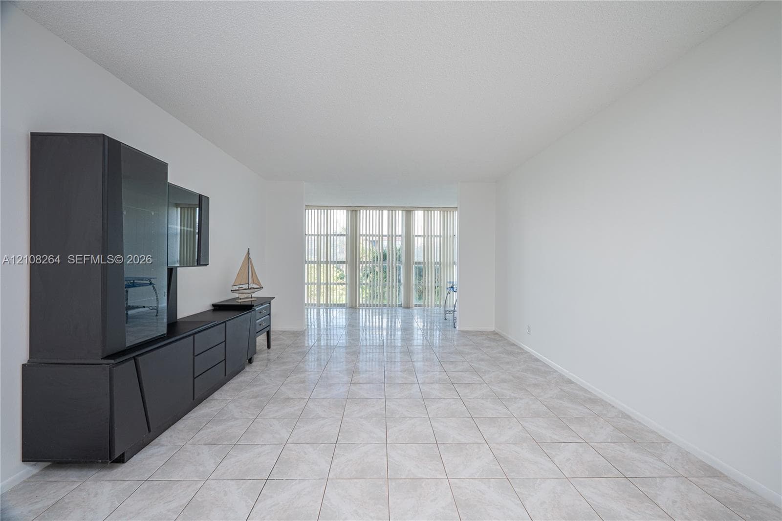 Open-concept living space featuring neutral ceramic tile flooring, floor-to-ceiling windows, and vertical blinds