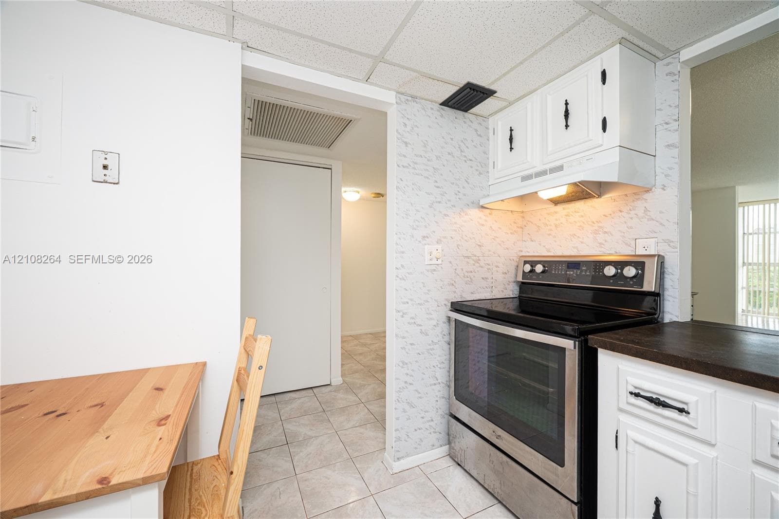 Kitchen area featuring white cabinetry with dark hardware, dark countertop, stainless steel range, and tile flooring