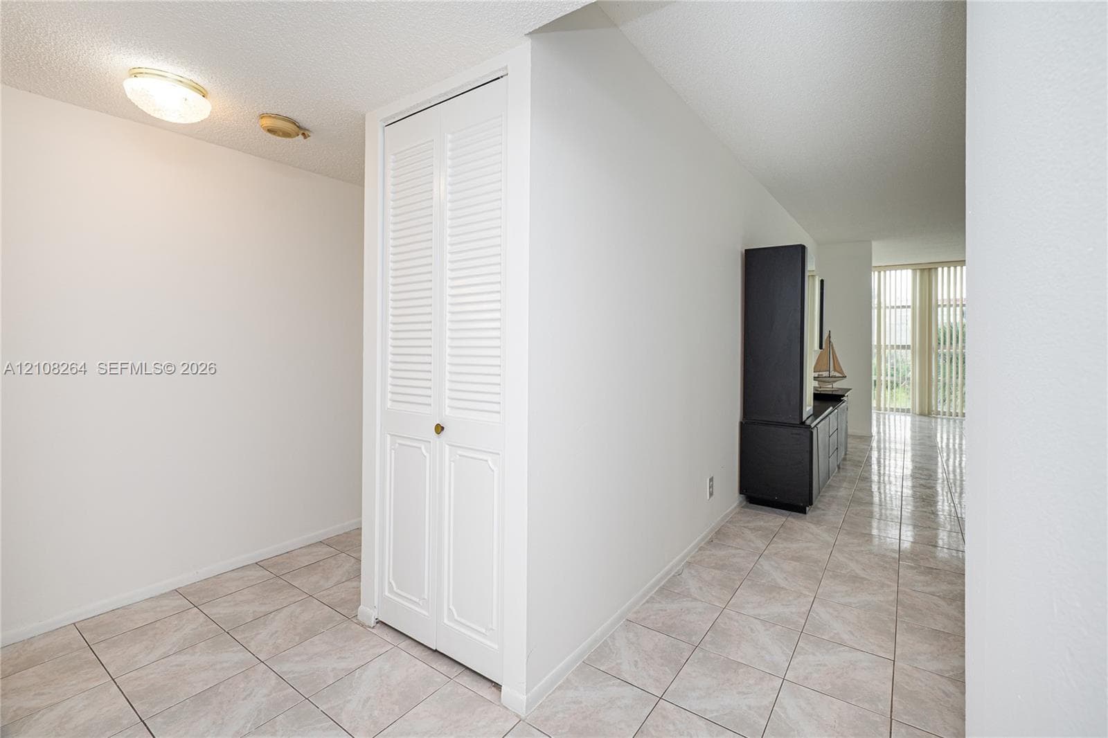 Neutral ceramic tile flooring, white louvered-panel closet doors, and floor-to-ceiling vertical blinds