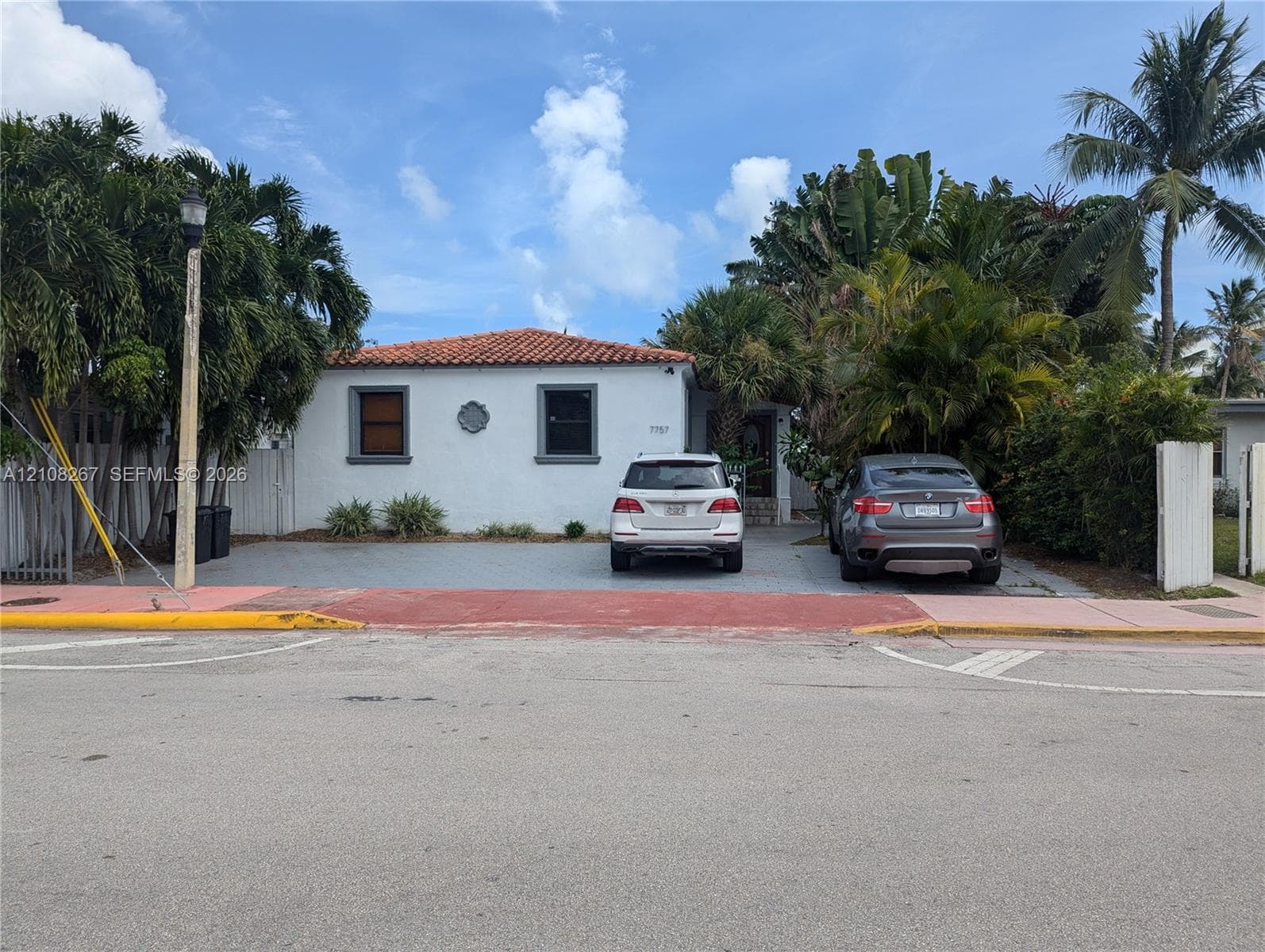Stucco exterior featuring a terracotta tile roof, paved driveway, and mature landscaping