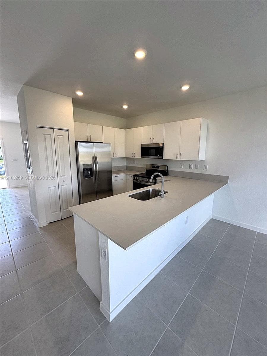 Kitchen featuring white flat-panel cabinetry, a peninsula with a stainless steel sink, quartz countertops, recessed lighting, and large-format tile flooring