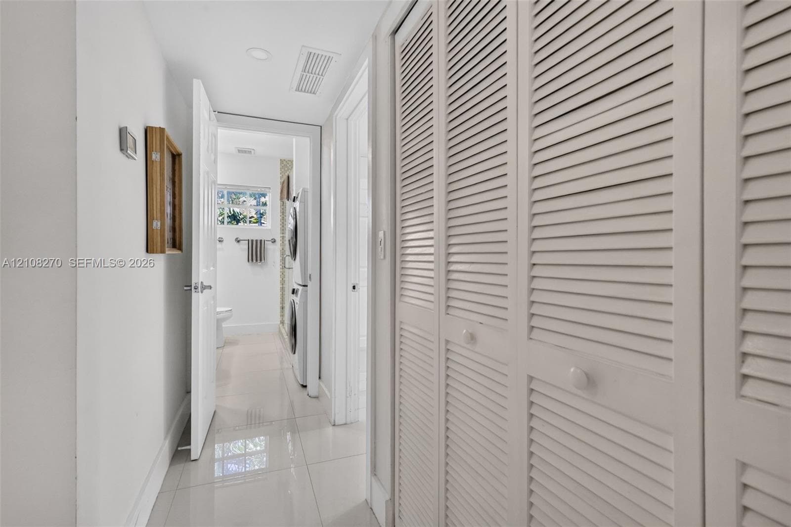 Hallway featuring full-height louvered closet doors, polished tile flooring, and recessed ceiling lighting