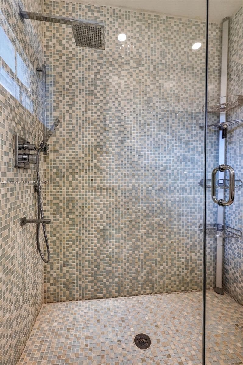 Walk-in shower featuring glass enclosure, mosaic tile wall surround, rainfall showerhead, handheld sprayer, and built-in corner shelving