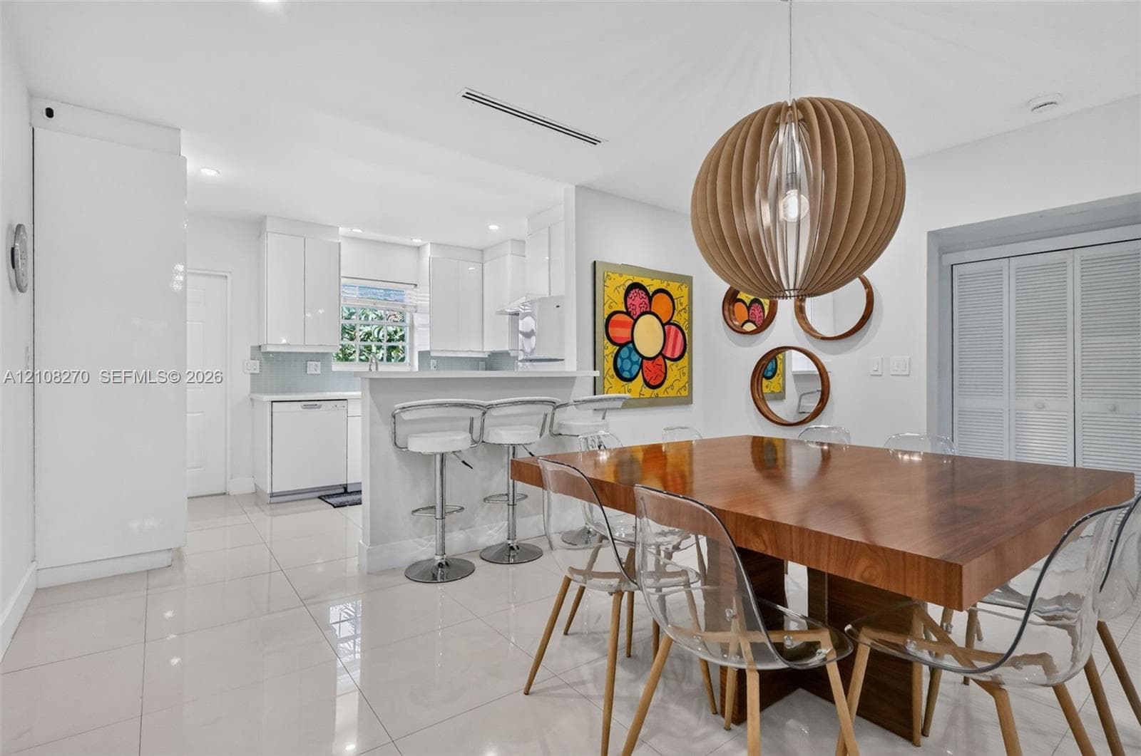 Kitchen featuring high-gloss cabinetry, stone-finish countertops, porcelain tile flooring, and a breakfast bar, complemented by a statement spherical wood-slat pendant light