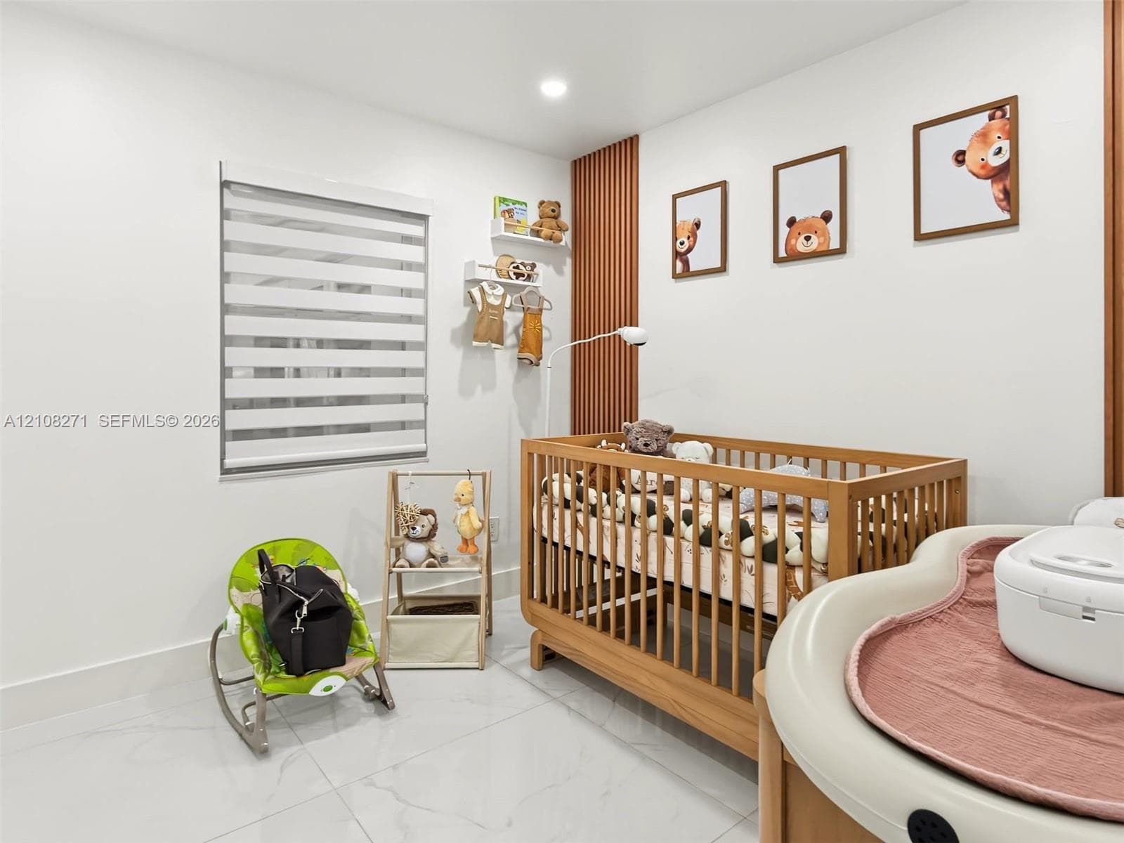 Bedroom featuring large-format light-toned tile flooring, recessed ceiling lighting, vertical wood-slat accent wall detailing, and a multi-layered light-filtering window shade