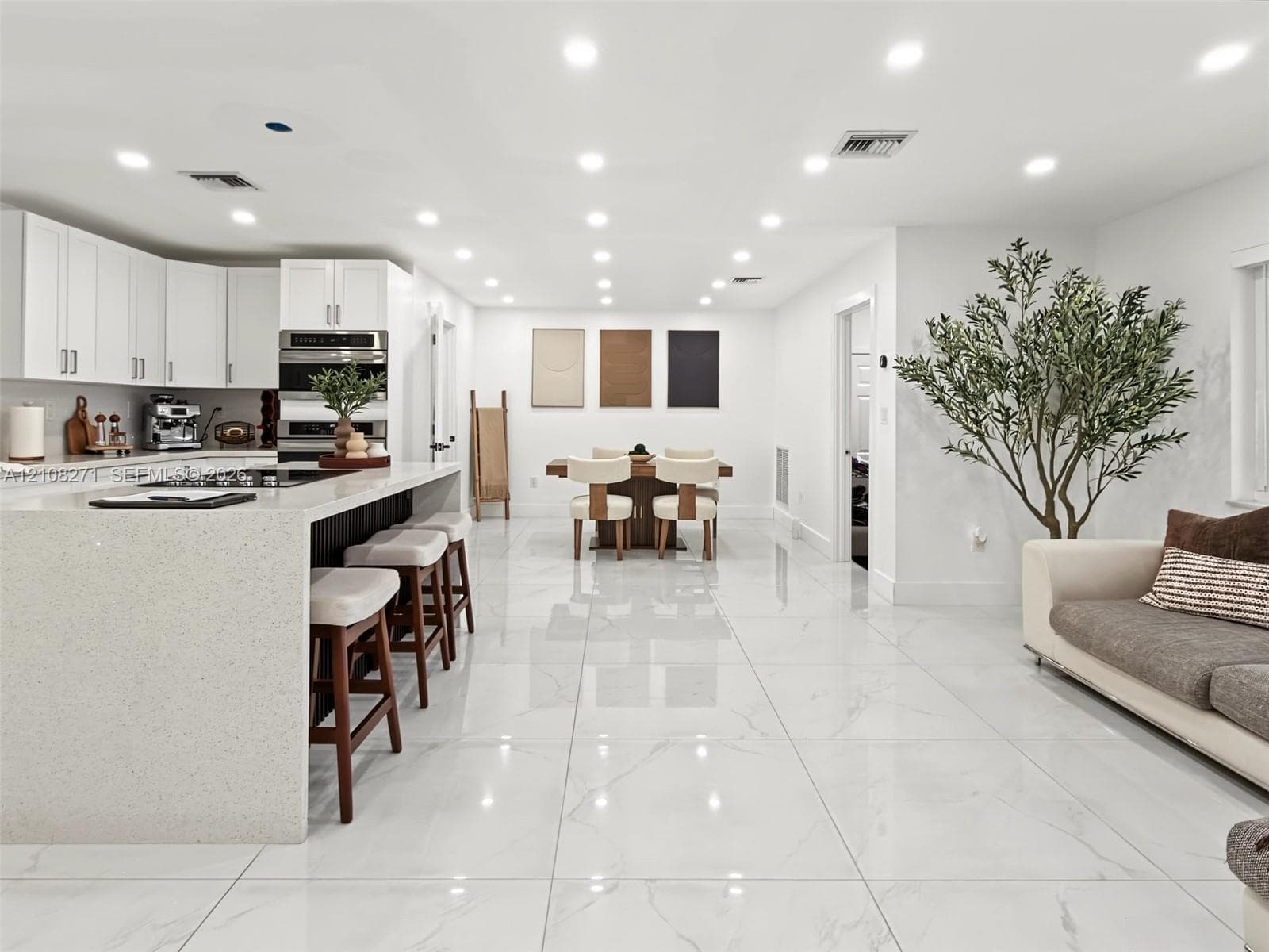 Open-concept kitchen featuring white shaker-style cabinetry, quartz countertops, a large island with integrated cooktop, recessed lighting, and large-format porcelain tile flooring
