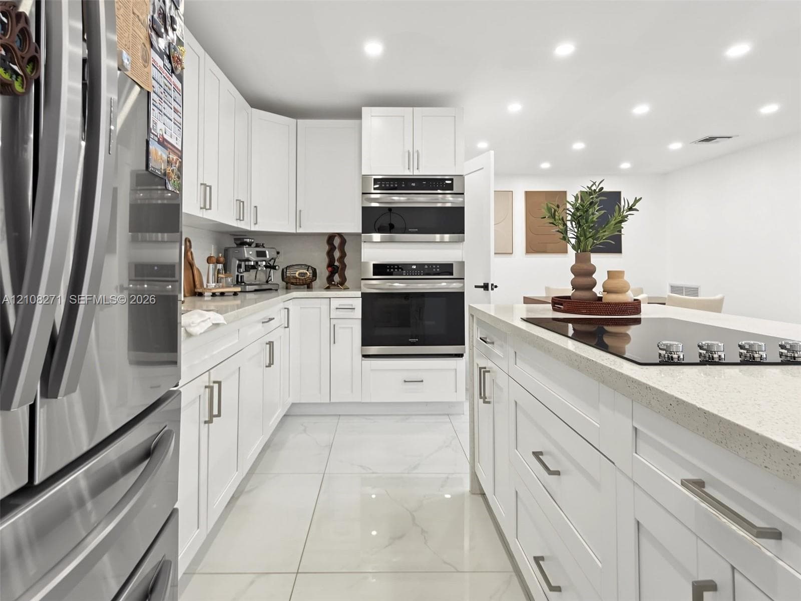 Kitchen featuring white Shaker-style cabinetry, a central island with a cooktop, stone-finish countertops, stainless steel wall-mounted double ovens, and large-format porcelain tile flooring