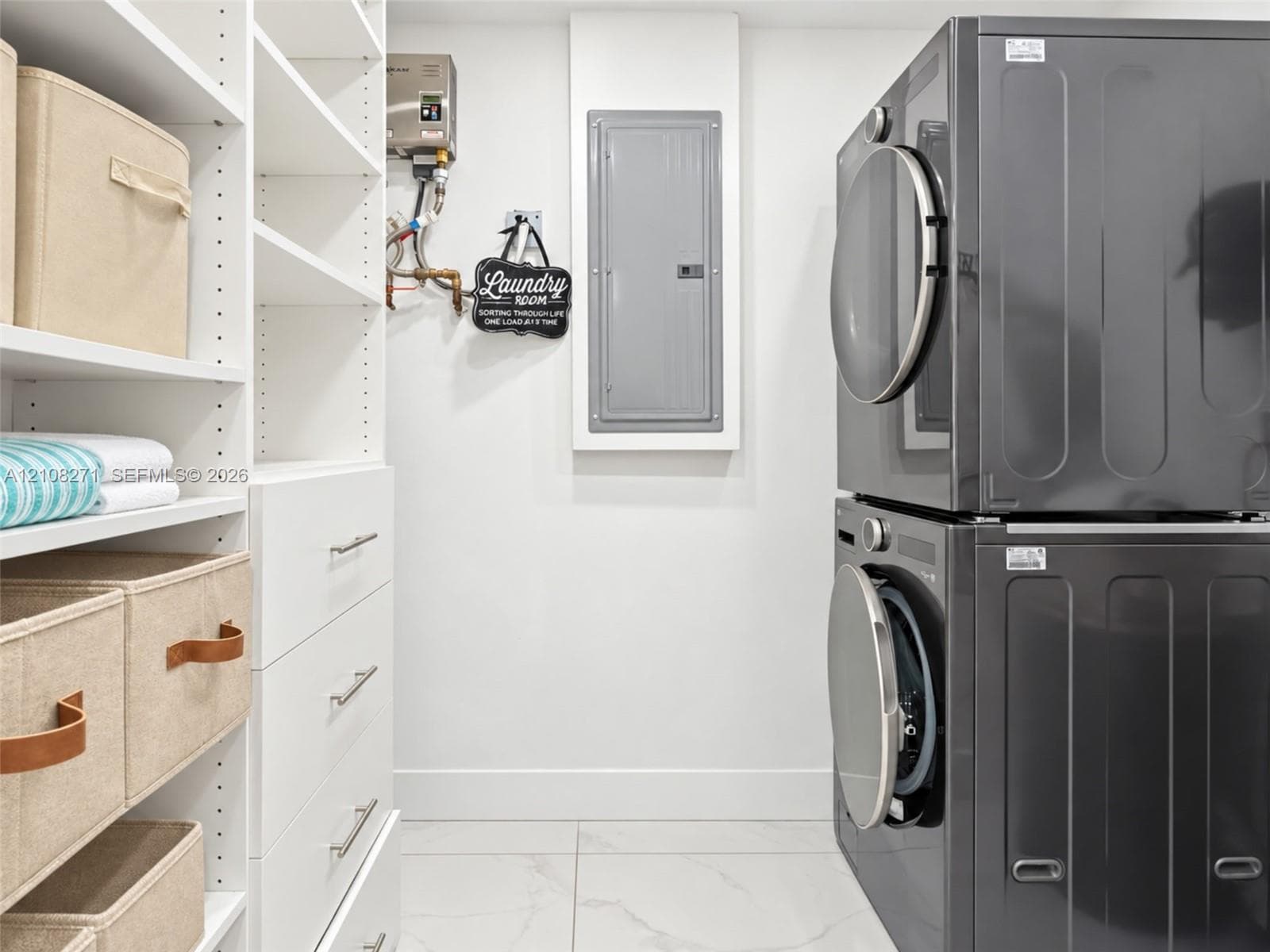 Laundry area featuring white built-in cabinetry with drawers, adjustable open shelving, large-format tile flooring, and stacked laundry appliances