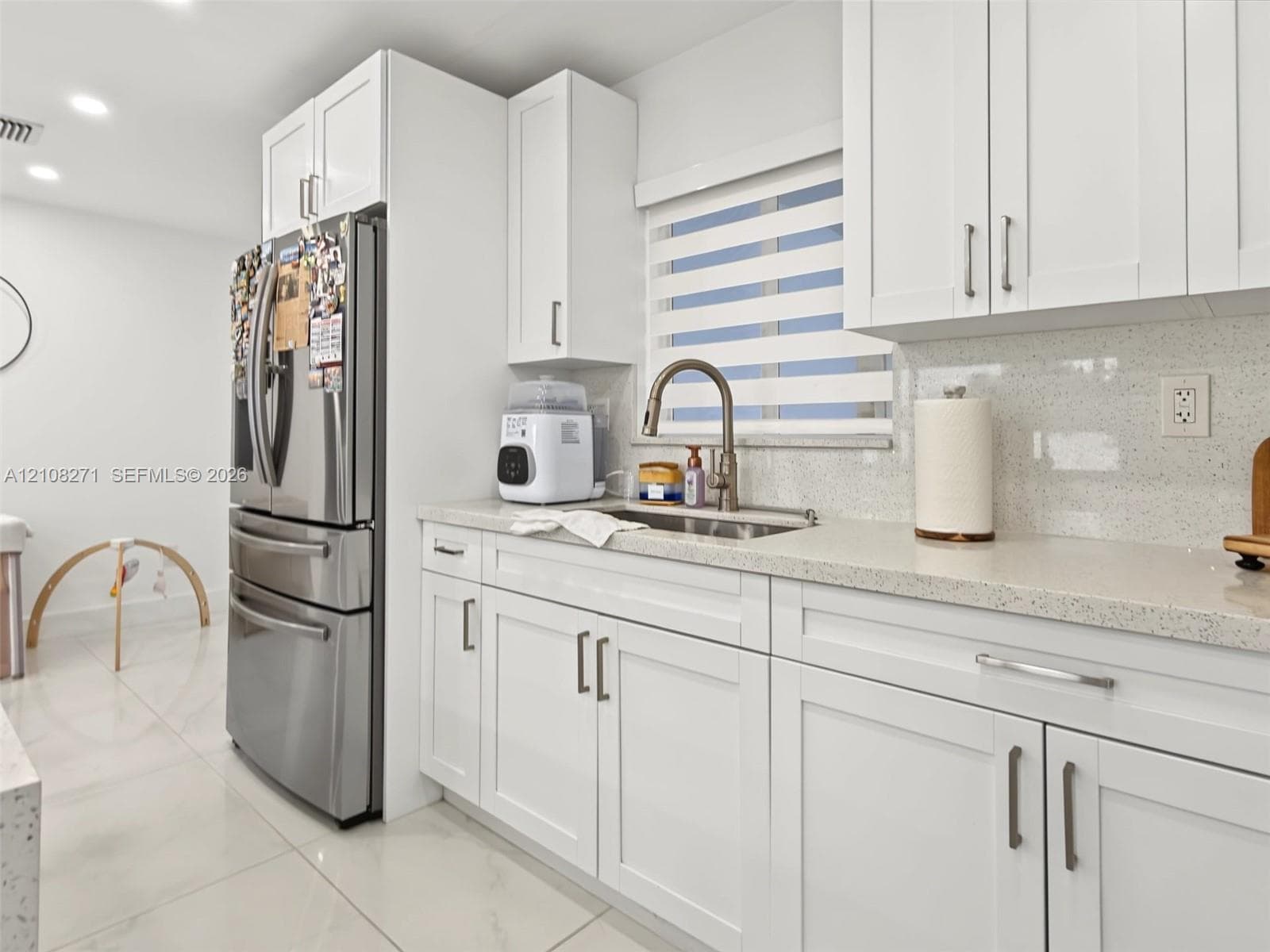 Kitchen featuring white shaker-style cabinetry, solid-surface countertops, a stainless steel french-door refrigerator, an undermount sink with a gooseneck faucet, and light-toned tile flooring