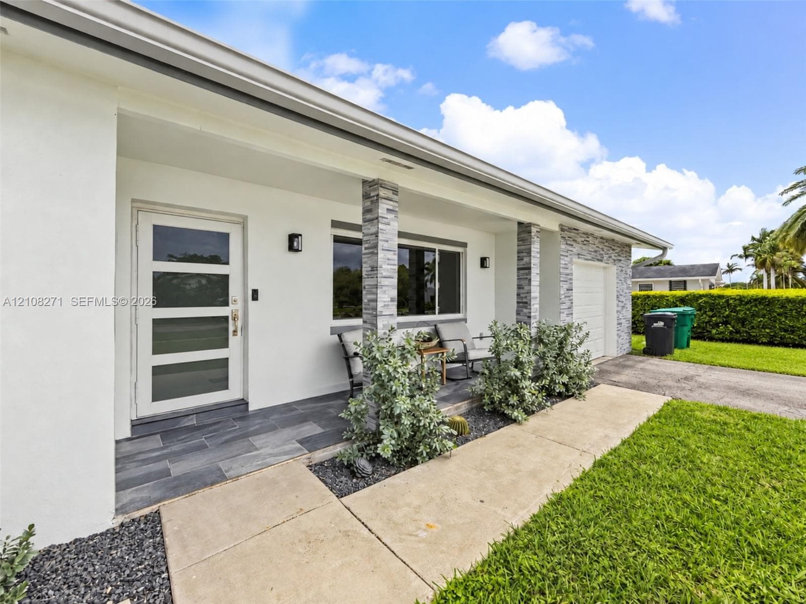 Exterior featuring a covered porch with large-format slate-finish tile flooring, stacked stone column cladding, a multi-pane glass entry door, and a matching stone-accented facade
