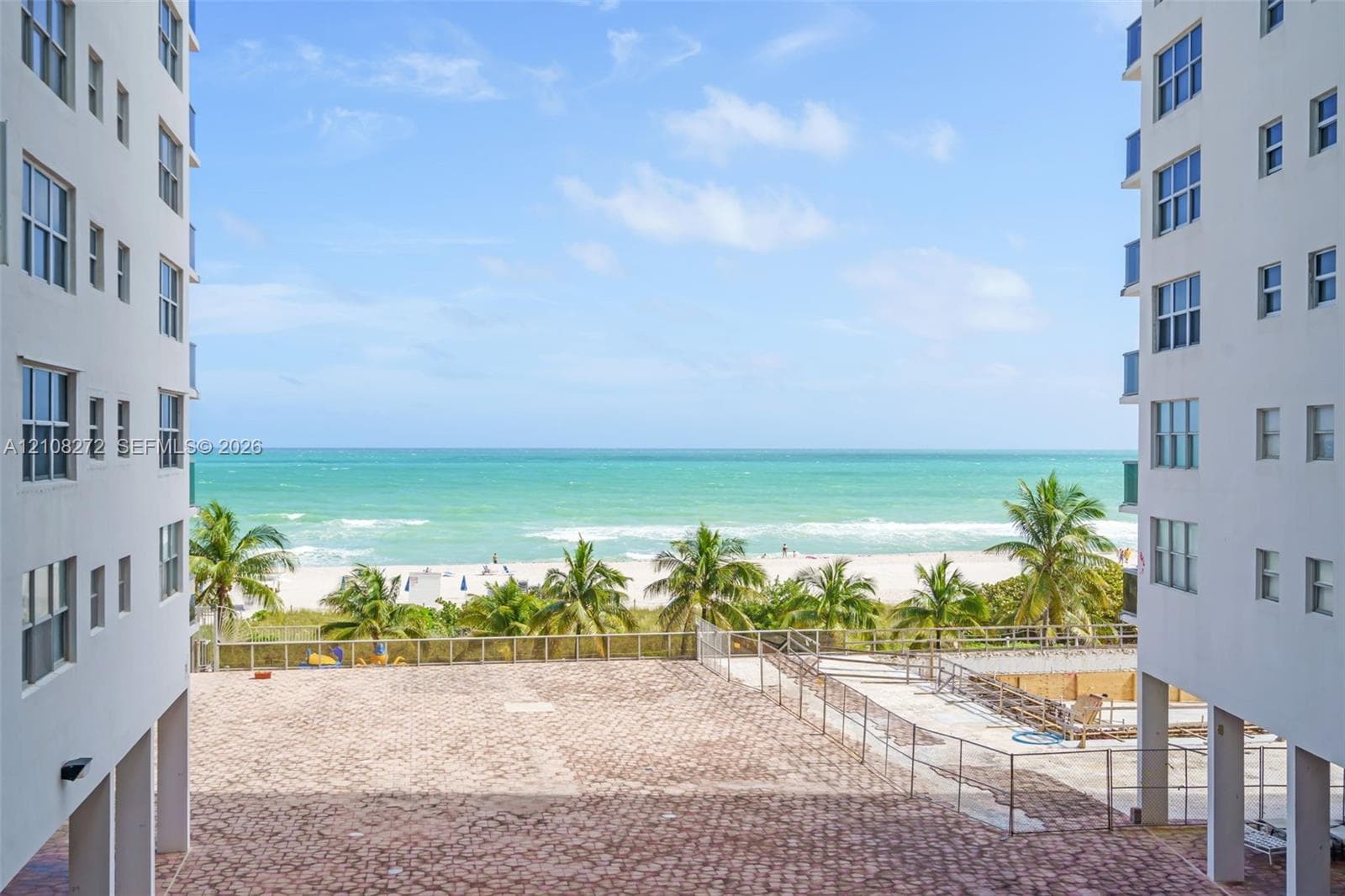 Paved plaza featuring perimeter metal fencing and direct oceanfront access to the sandy beach and coast