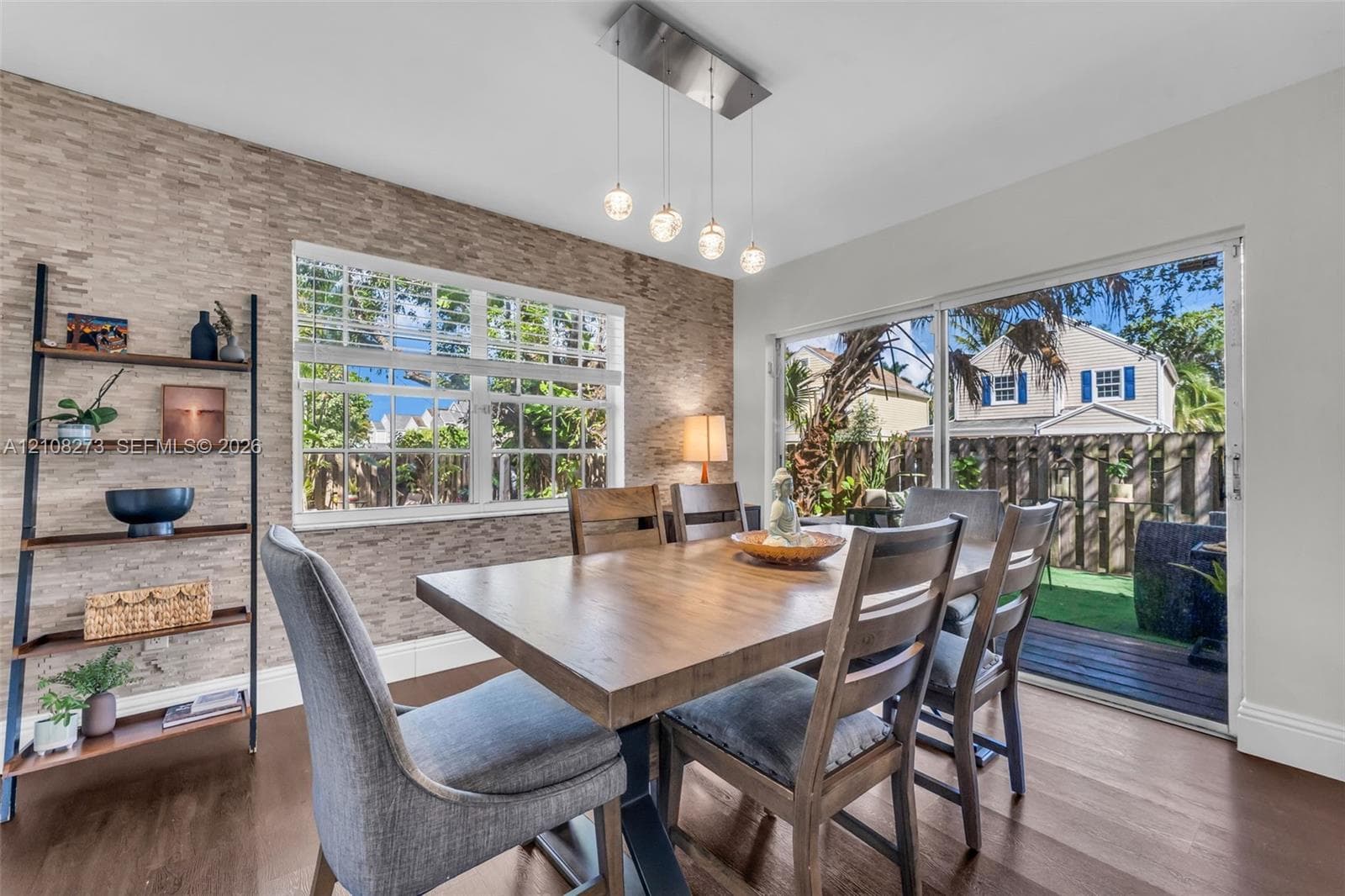 Textured stone accent wall, multi-light pendant fixture, grid-patterned windows, wood-finish flooring, and sliding glass doors