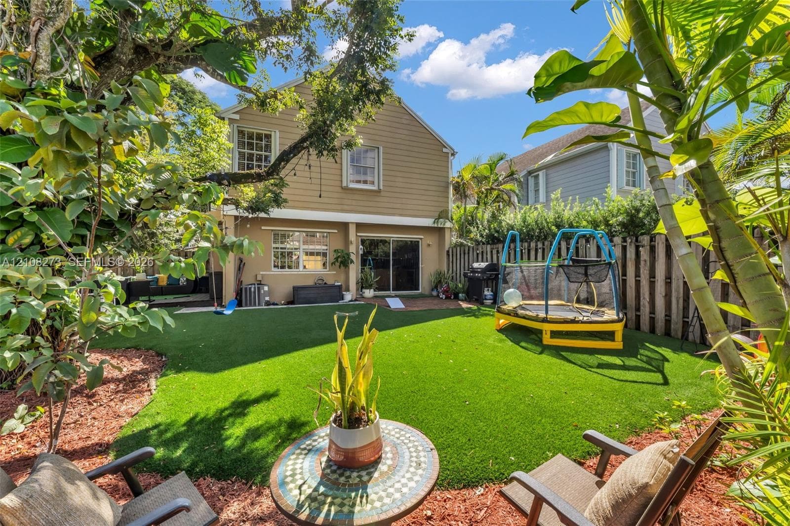 Fenced backyard featuring synthetic turf, wood-siding exterior, and mature landscape