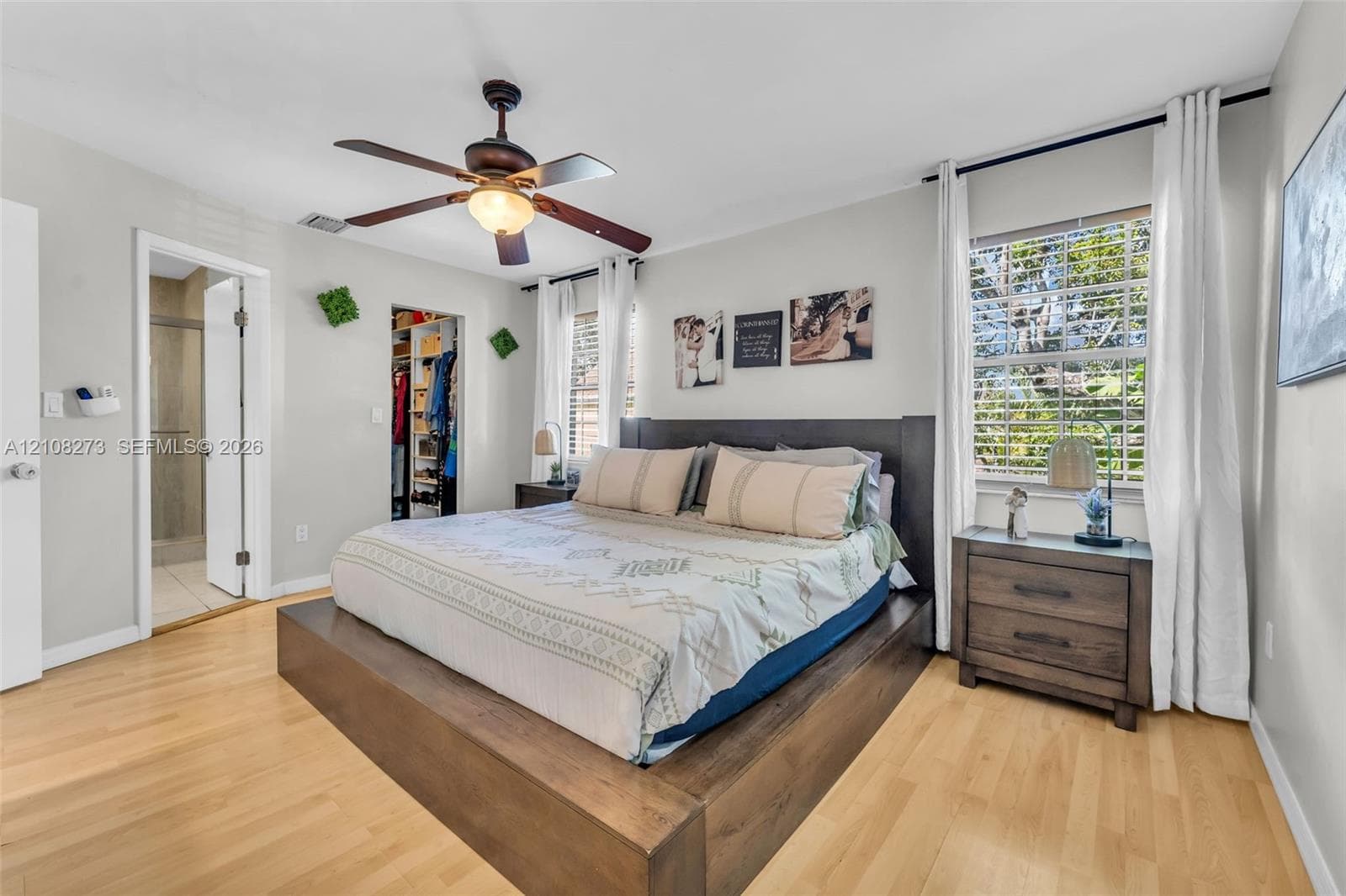 Bedroom featuring light wood-finish flooring, a ceiling fan with integrated lighting, and a walk-in closet with built-in organization