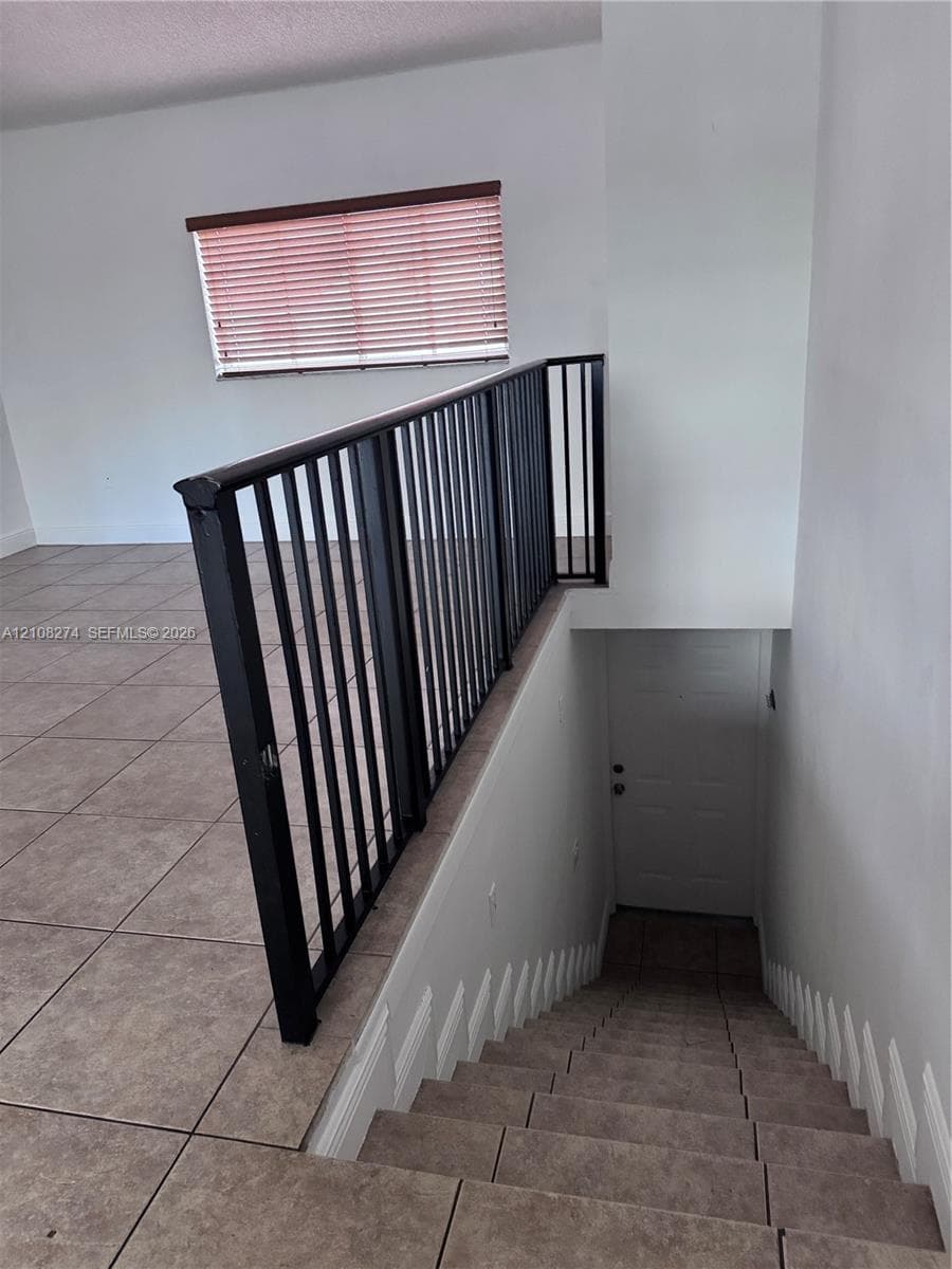 Staircase featuring tile treads and a black metal handrail