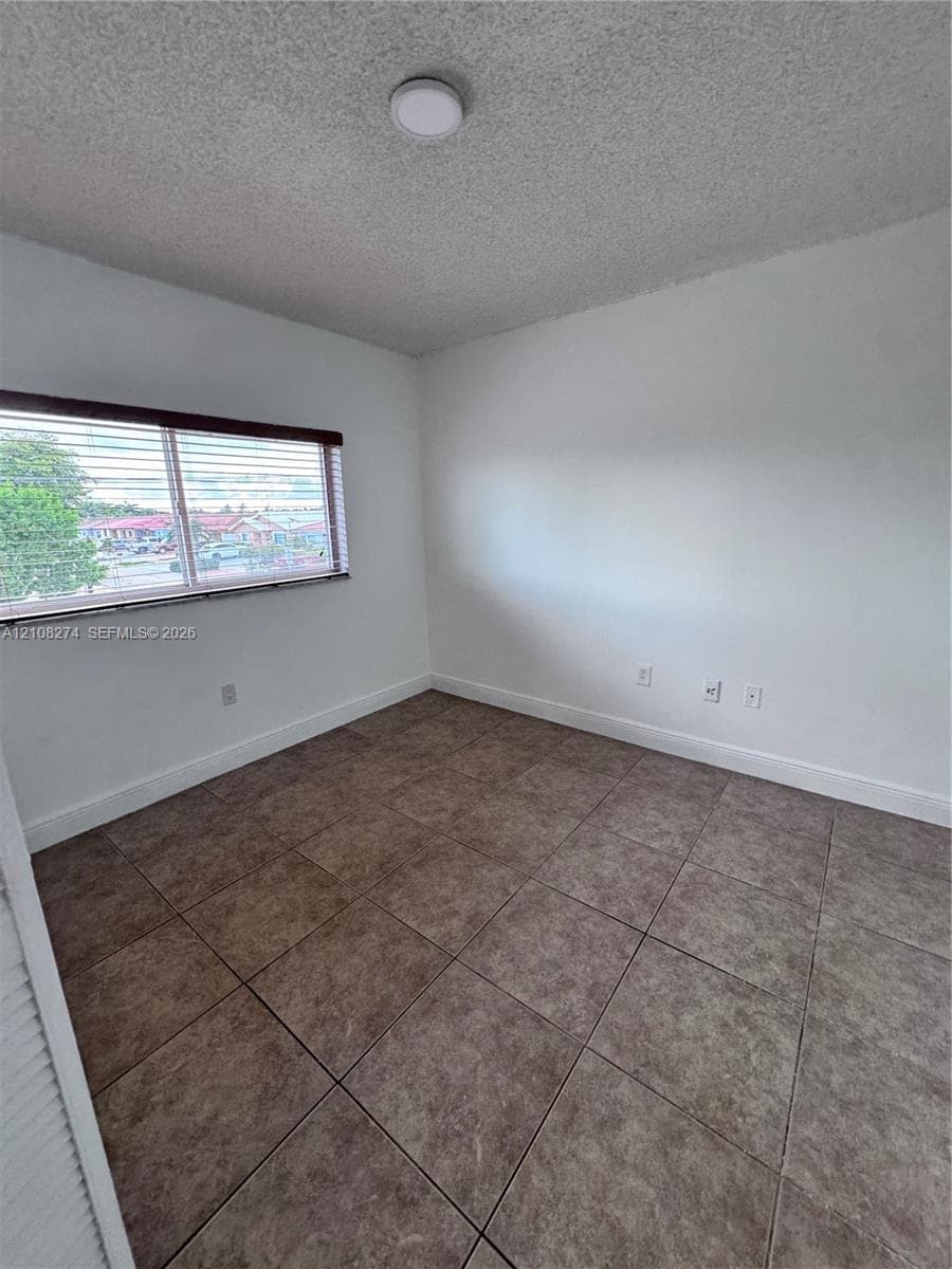 Interior space featuring white walls,ceramic tile flooring, a dual-pane horizontal sliding window with attached blinds, and a circular flush-mount ceiling light fixture