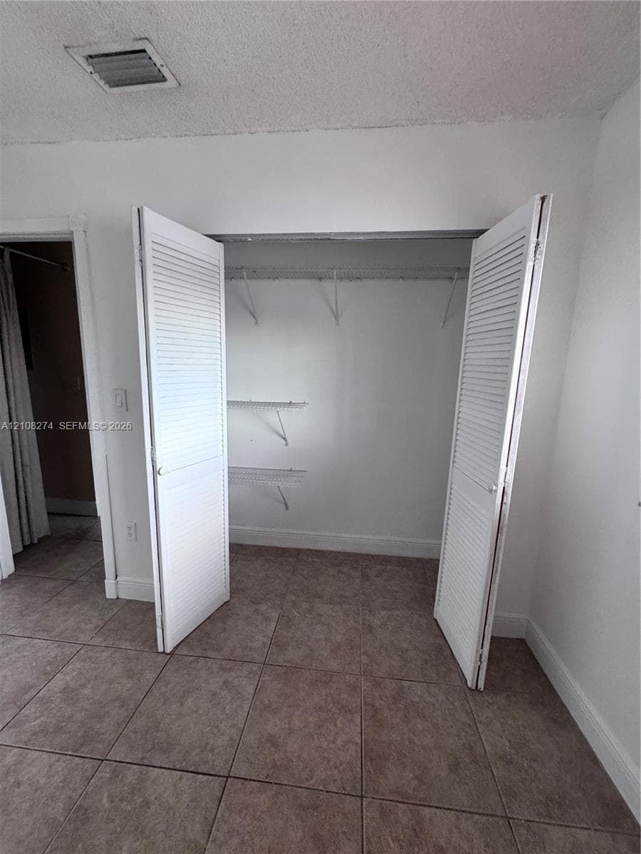 Closet featuring white louvered bifold doors and built-in wire shelving units, complemented by neutral tile flooring