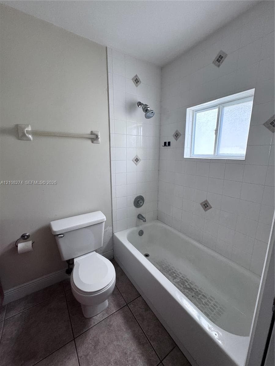 Bathroom featuring a porcelain soaking tub, white ceramic wall tile with decorative accents, an integrated showerhead, and tile flooring