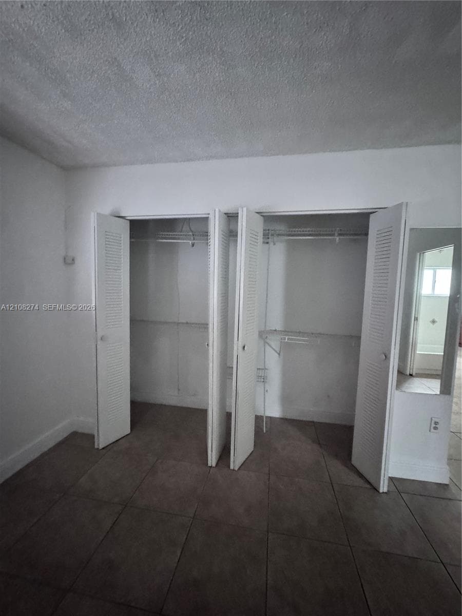Dual closets featuring white louvered doors, wire shelving, and neutral tile flooring