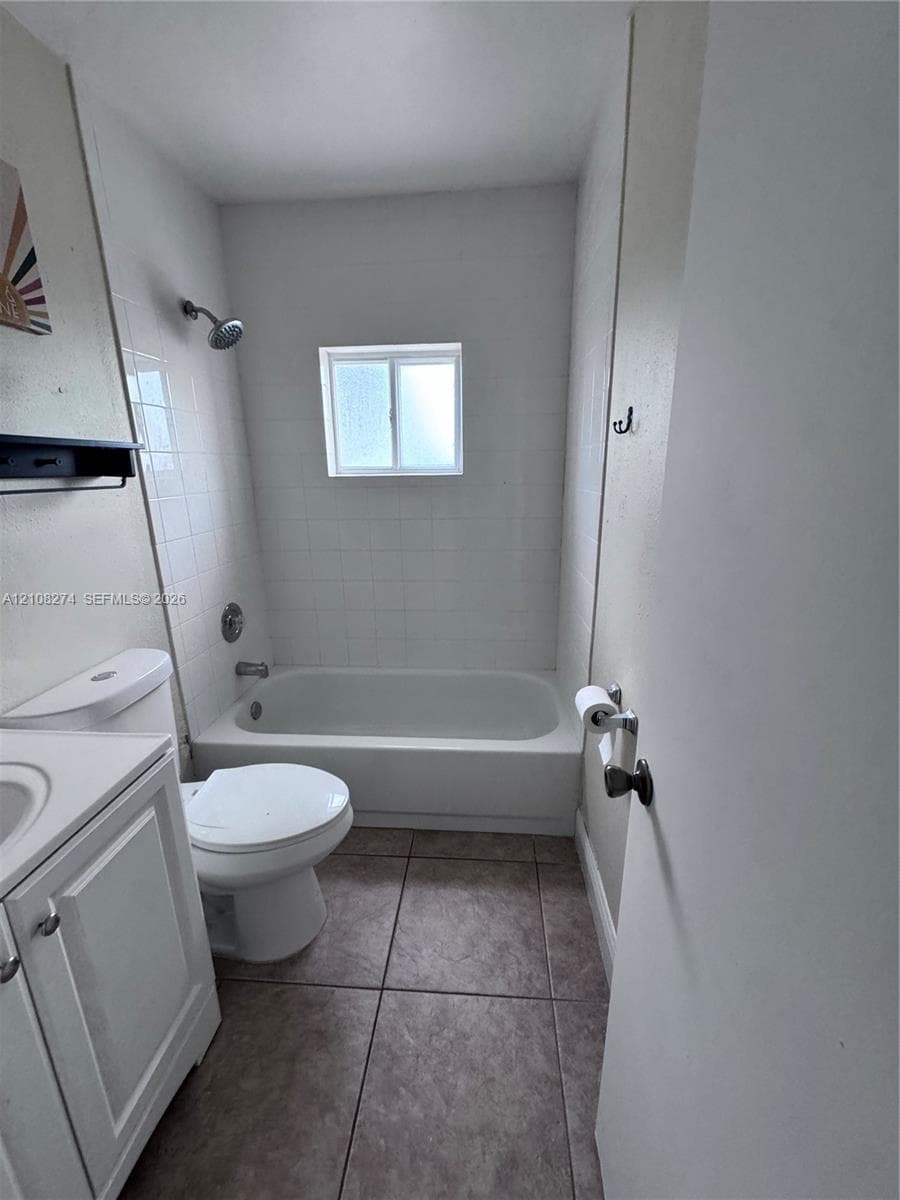 Bathroom featuring tile flooring, a bathtub-shower combination with white wall tile, a single-door vanity cabinet, and a sliding window