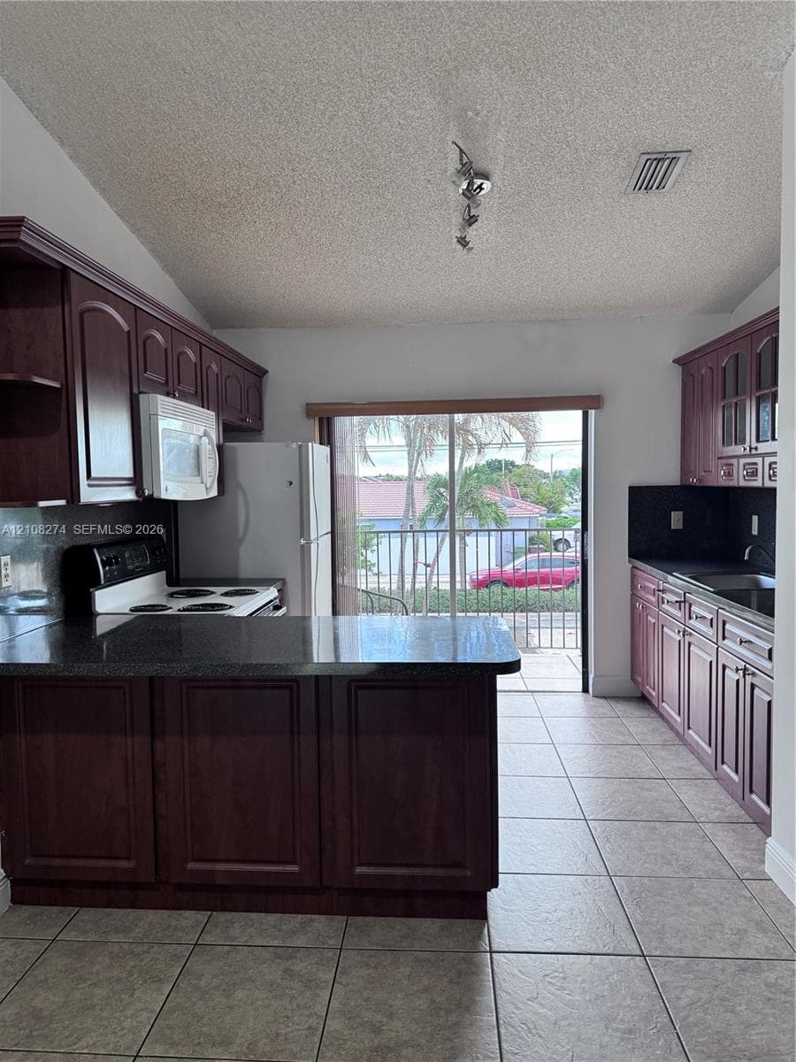 Kitchen featuring dark-toned cabinetry, dark countertops, a peninsula, tile flooring, and a sliding glass door