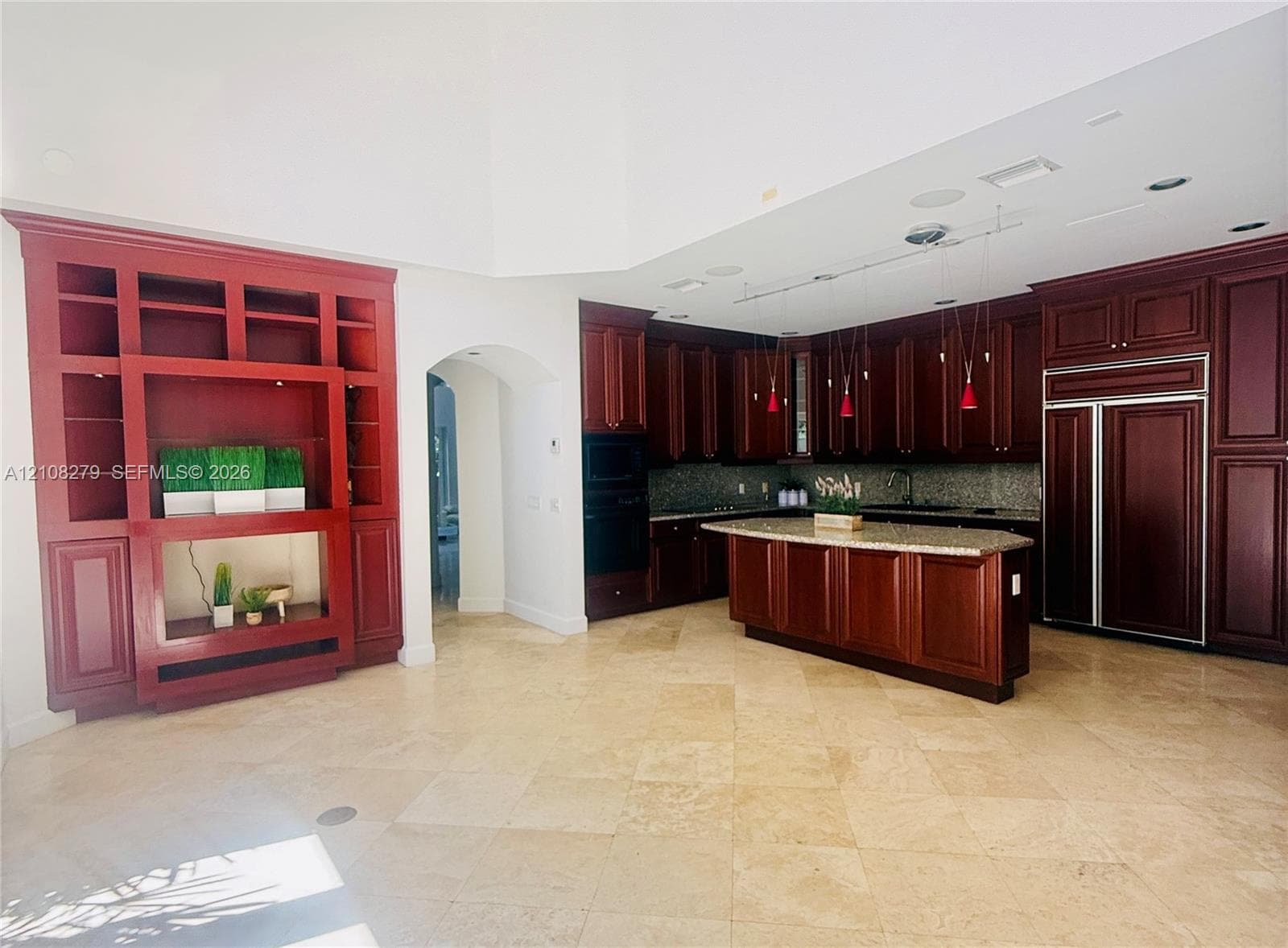 Kitchen featuring custom stained-wood cabinetry, stone countertops, central island, built-in panel-ready refrigerator, and stone tile flooring