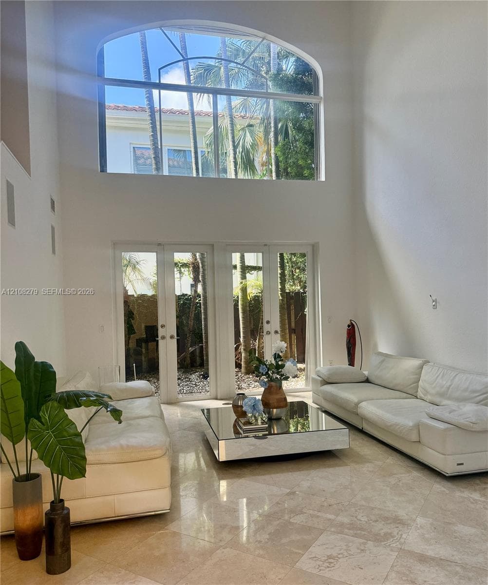 Double-height living area featuring floor-to-ceiling arched windows, stone tile flooring, and dual sets of glass-paned doors