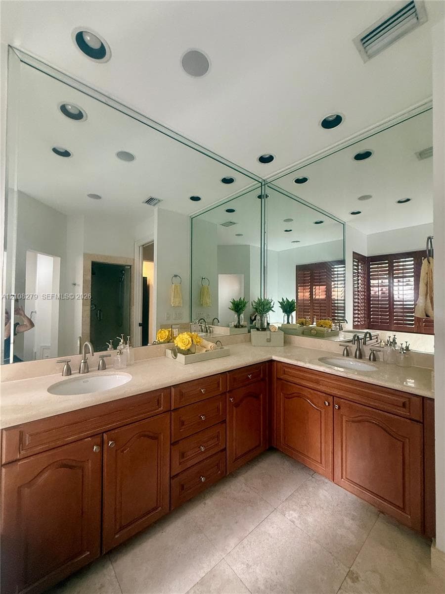 L-shaped vanity featuring raised-panel wood cabinetry, light-toned stone-finish countertops, dual integrated undermount sinks, and full-height wall mirrors