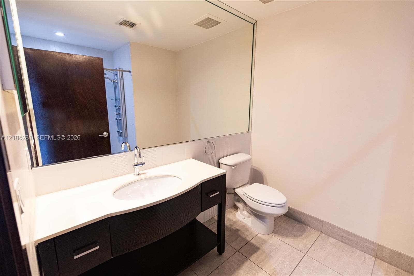 Bathroom featuring a vanity with a white countertop and oval under-mount sink, full-width wall mirror, and large-format tile flooring