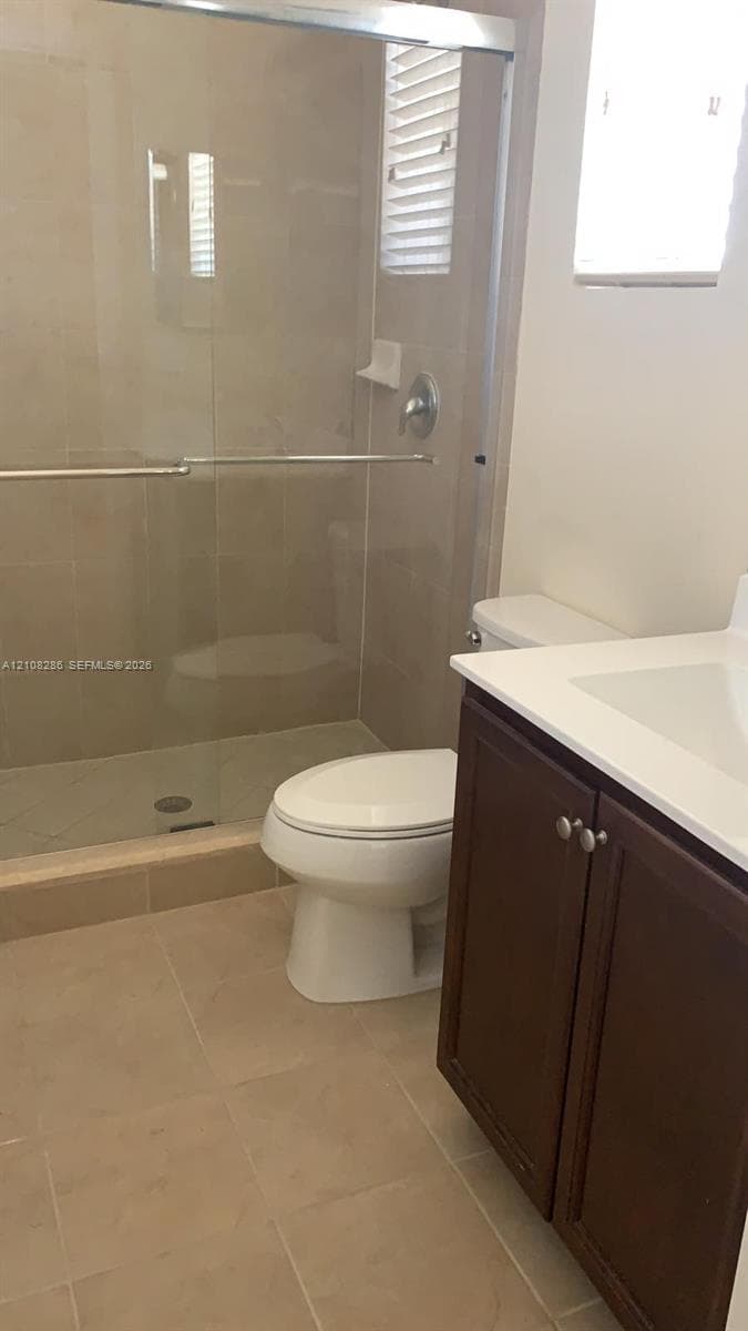 Bathroom featuring a glass-enclosed shower with tiled surround, stone-composite countertop, dark wood-finish cabinetry, and neutral floor tiling