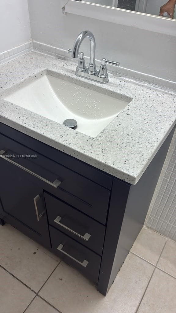 Bathroom vanity featuring a dark-finish cabinet with satin nickel hardware, a speckled composite countertop, an integrated rectangular sink, and a high-arc chrome faucet