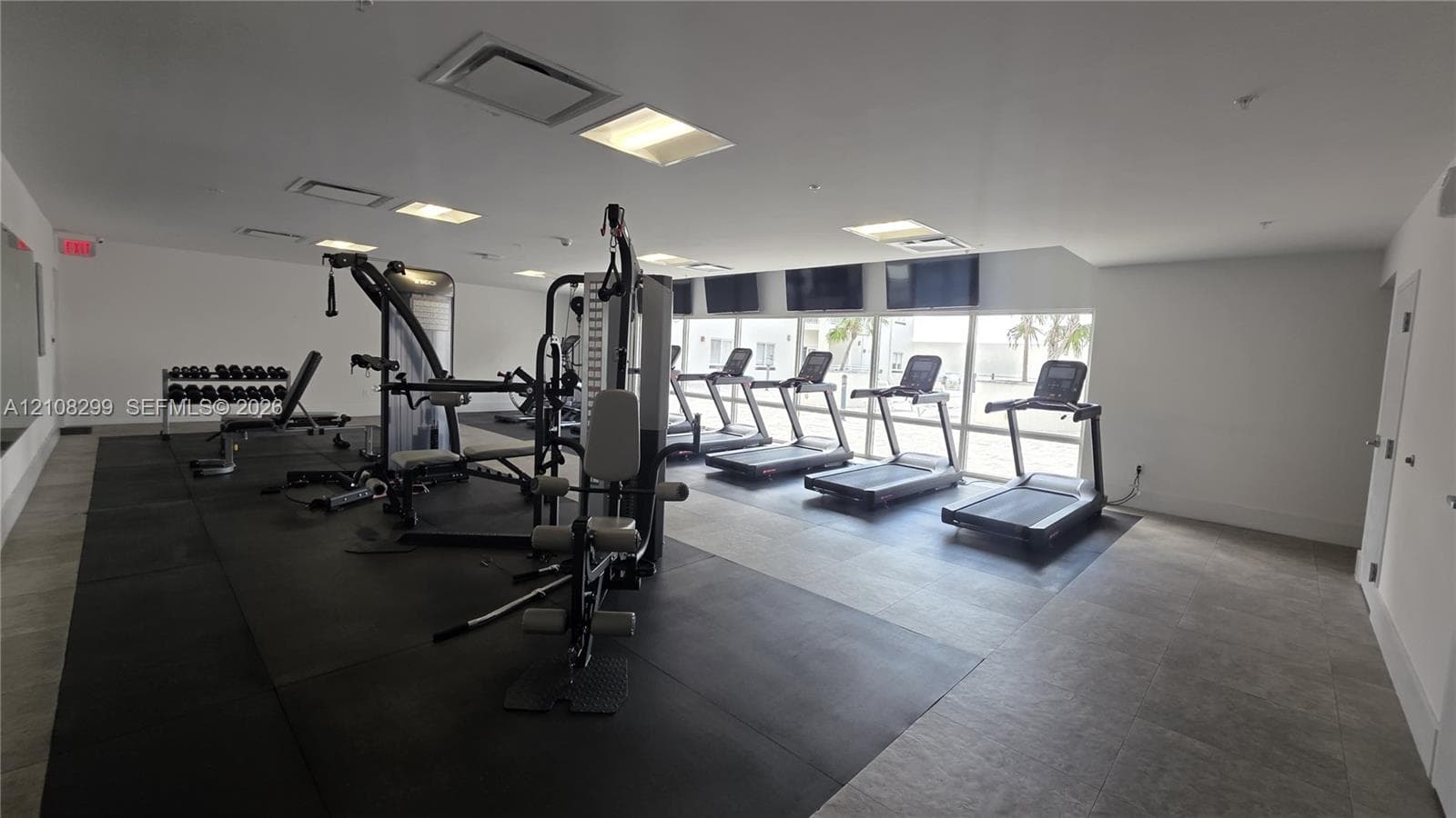 Fitness center featuring ceramic tile flooring, rubber exercise matting, recessed lighting, and wall-mounted televisions