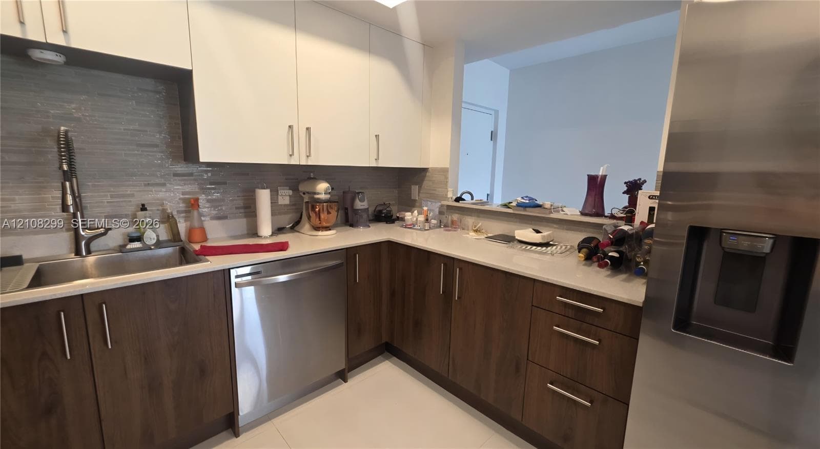 Kitchen featuring white upper cabinetry, dark wood-finish lower cabinetry, stone countertops, stainless steel appliances, and a horizontal tile backsplash
