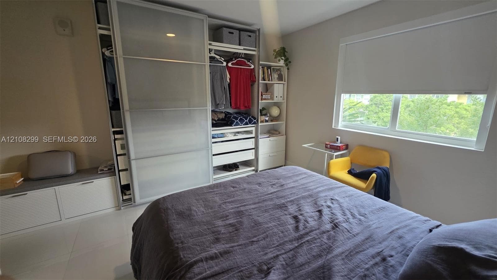 Built-in floor-to-ceiling wardrobe featuring sliding frosted-glass doors, integrated shelving, and drawers, accompanied by a low-profile storage bench and large-format tile flooring