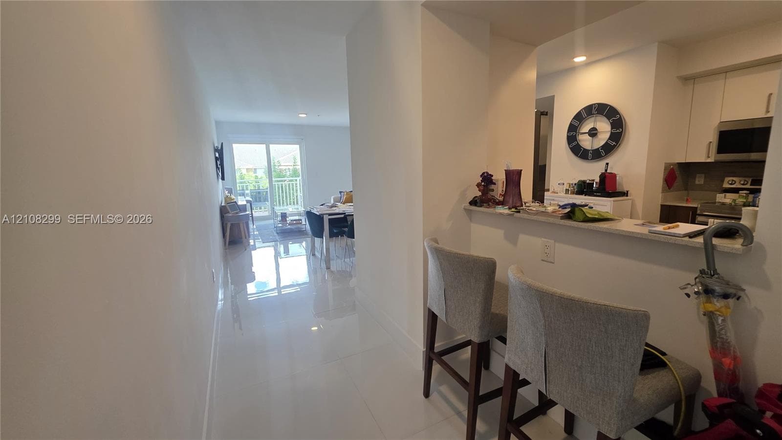 Kitchen featuring a pass-through breakfast bar with a solid surface countertop, white cabinetry, integrated microwave, and polished tile flooring