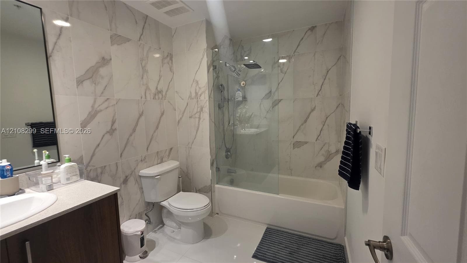 Bathroom featuring wall-to-wall stone-finish tile surround, glass shower panel, vanity with an integrated basin, and recessed lighting