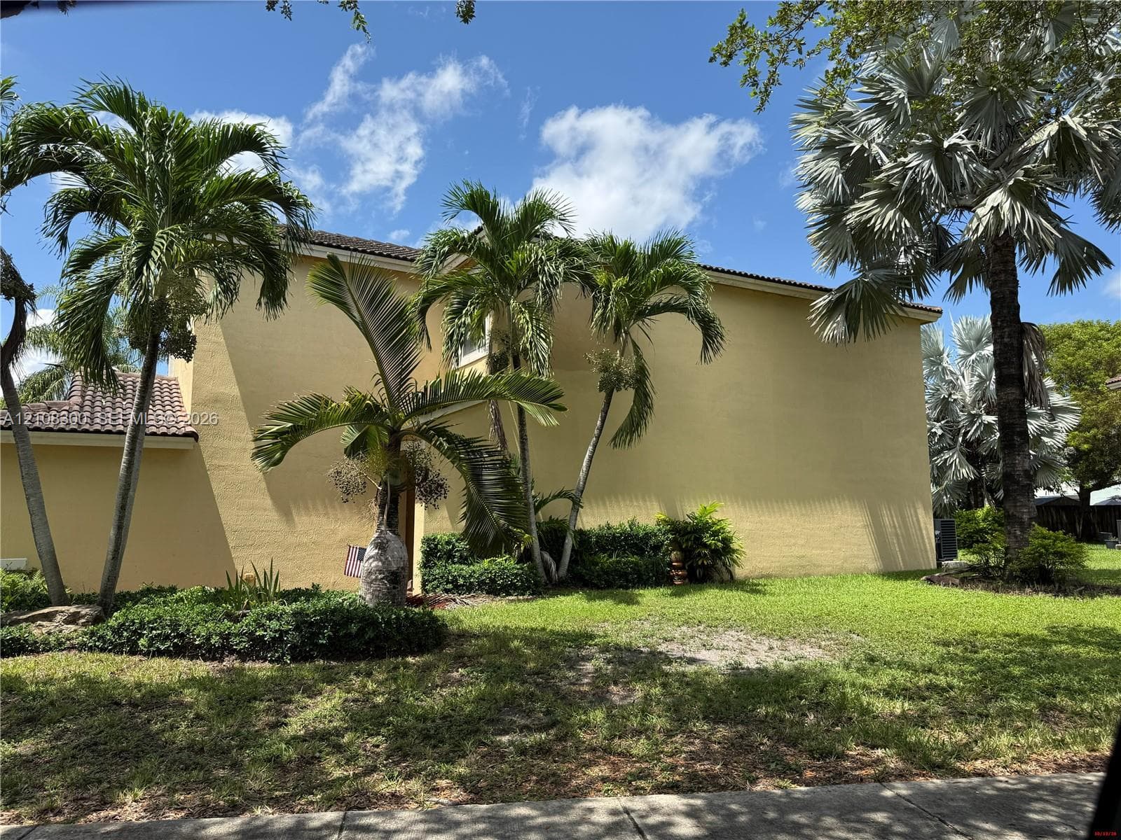Two-story stucco exterior featuring a tile roof, manicured lawn, and mature palm trees